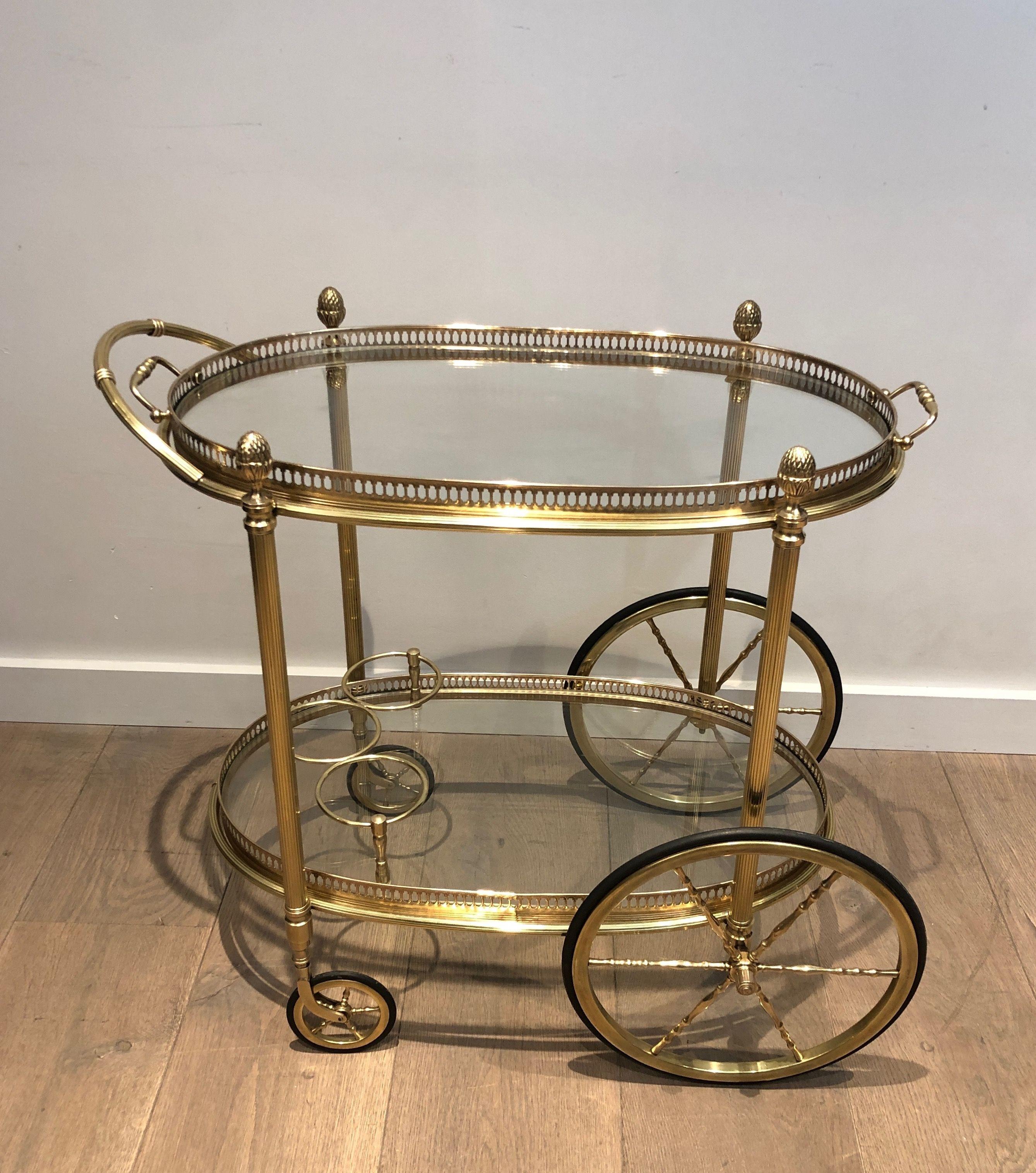 This neoclassical style oval bar cart is all made of brass. It has two removable oval trays made of glass and surrounded by a delicate brass gallery. This is a French work by famous designer Maison Bagués. Circa 1940.