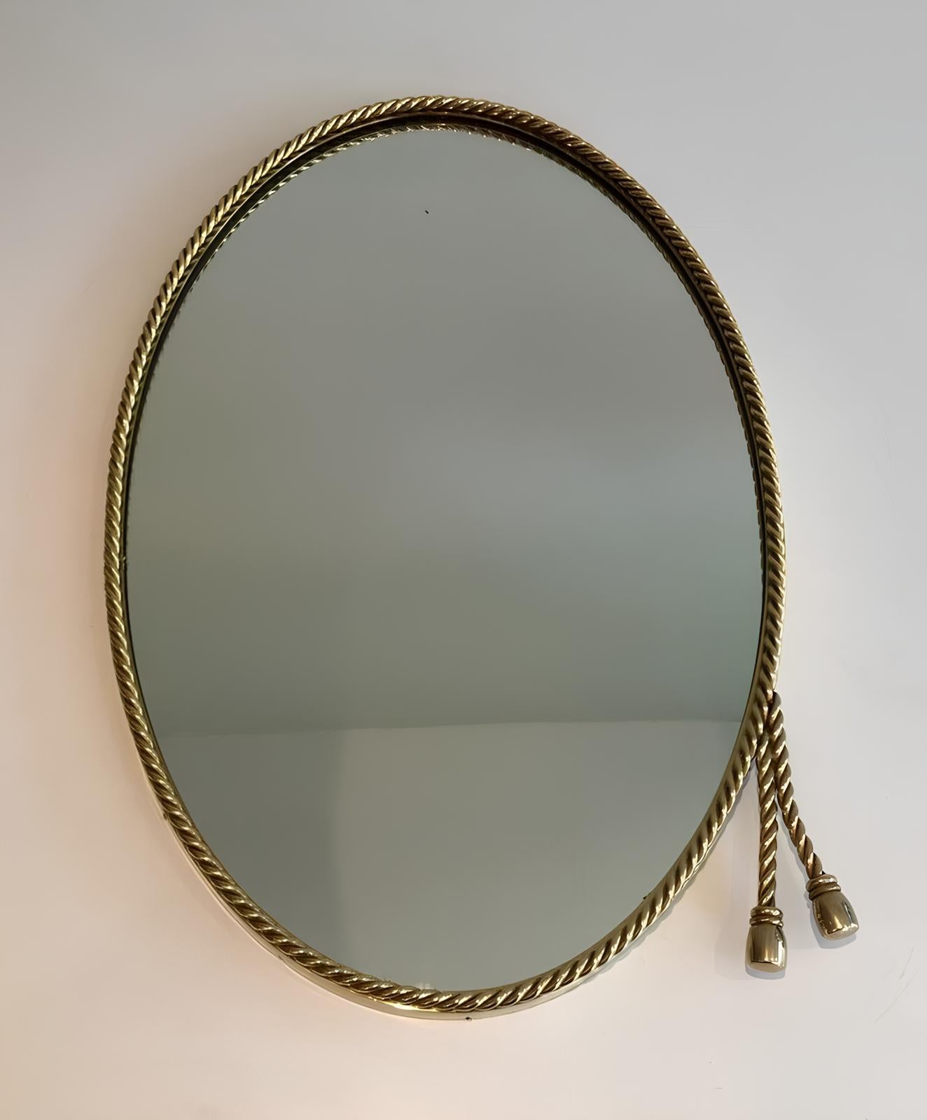 Este bonito espejo ovalado es de latón y está rodeado por un cordón decorado con 2 pompones. Se trata de una obra francesa al estilo de Maison Bagués. Alrededor de 1940