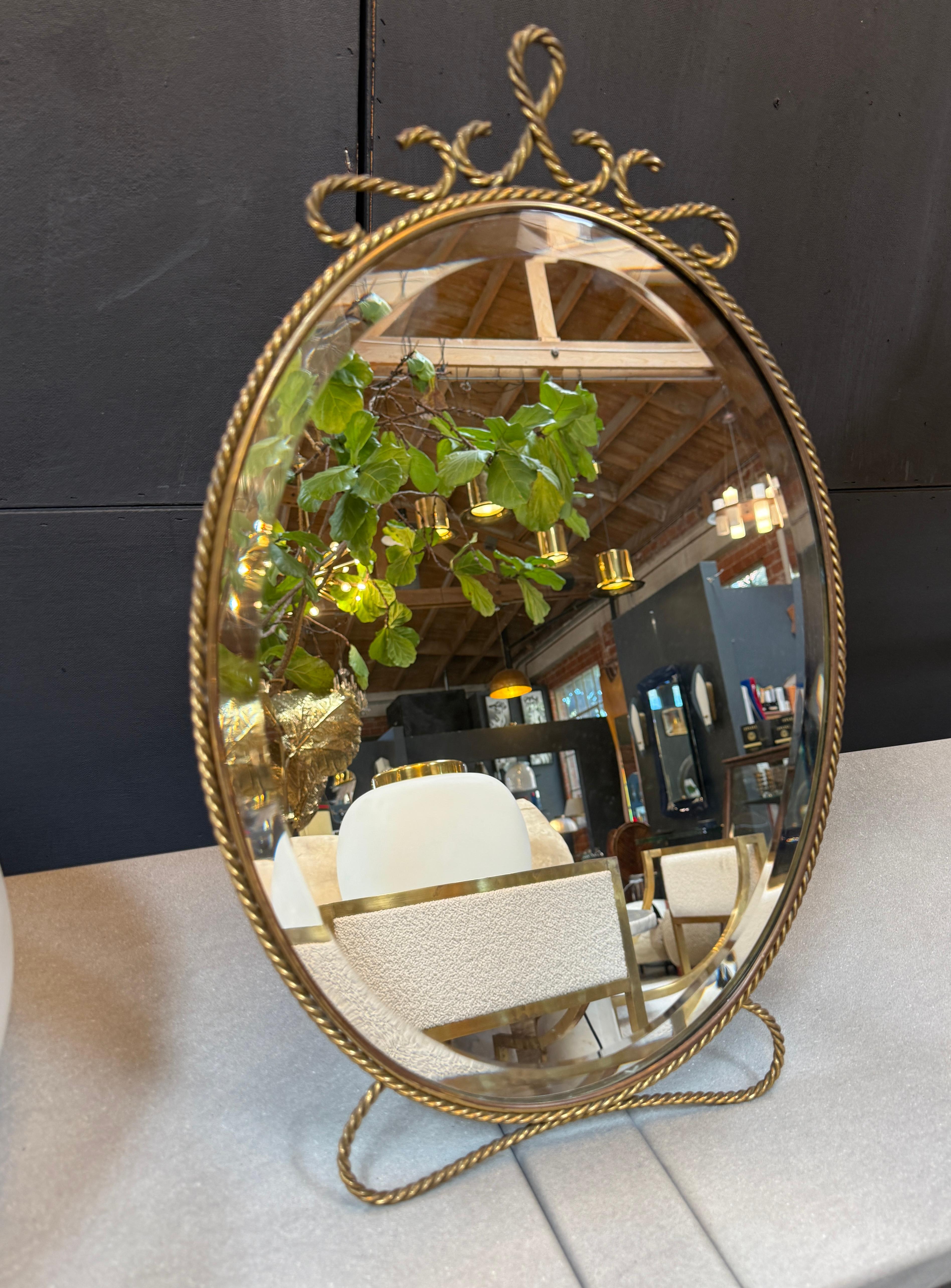 Elegant et intemporel, ce miroir de courtoisie ovale vintage présente un cadre en laiton magnifiquement détaillé avec une bordure en corde torsadée et une crête ornée de volutes. Ses tons dorés et chauds et son design classique en font un objet