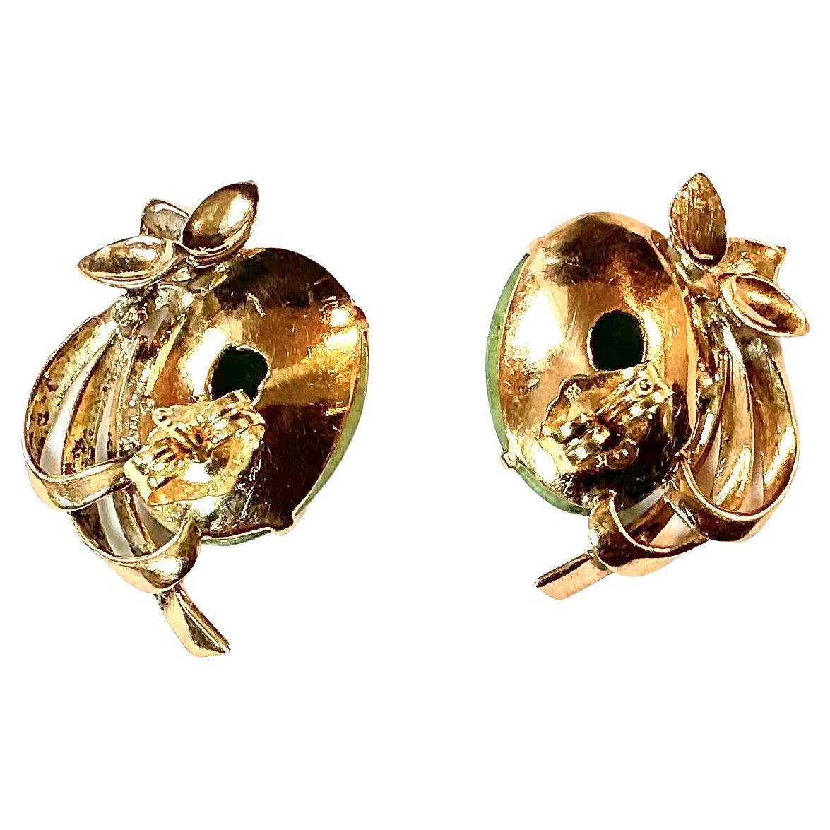 Pair of Mid-20th Century 14k Yellow Gold Jadeite Oval Cabochon Cut Earrings with Post Backs. Each earring showcases approximately 5 carats of oval jadeite gemstone, bezel set and accented by a graceful gold foliate motif and arched ribbon detailing.
