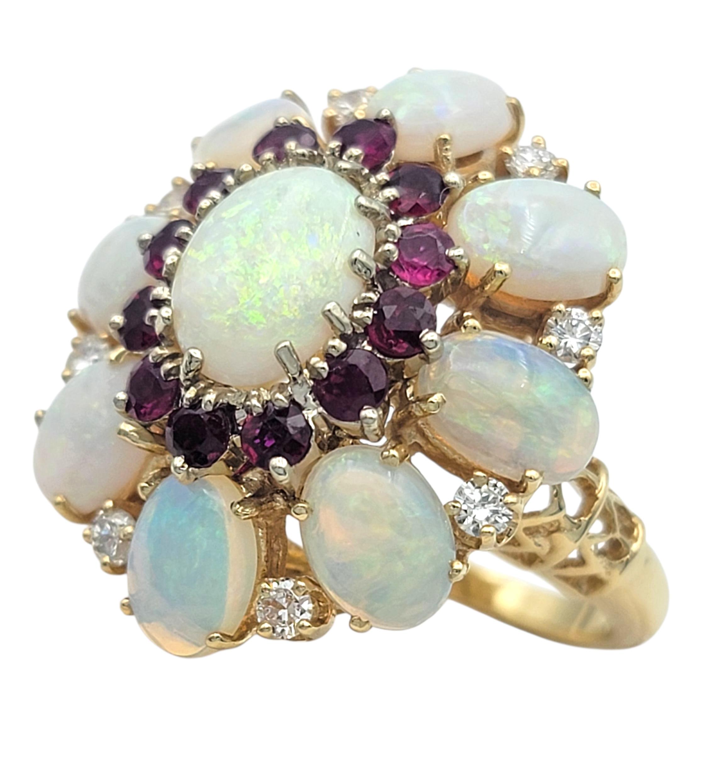 This captivating ring features a cluster design centered around a luminous oval opal that radiates flashes of pink, green, and blue. Surrounding the center opal are smaller opals, as well as alternating halos of rich red rubies and sparkling