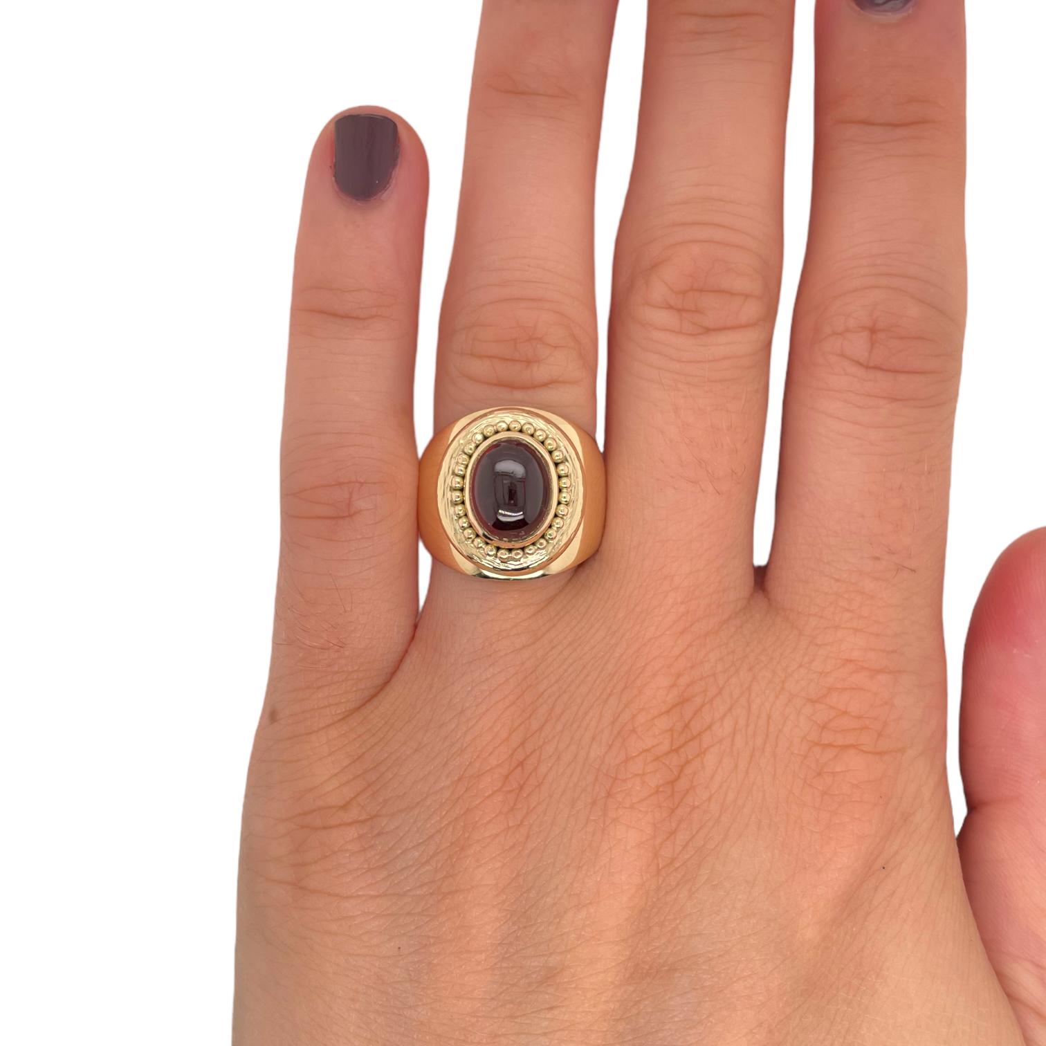Ring contains one center 9.7x7.7mm oval cabochon garnet, approximately 2.50cts. Surrounding oval garnet are 18K yellow gold bead accents. Widest part of ring measures 17.5mm. Ring weighs approximately 12.3 grams and is a size 6.75. Please request