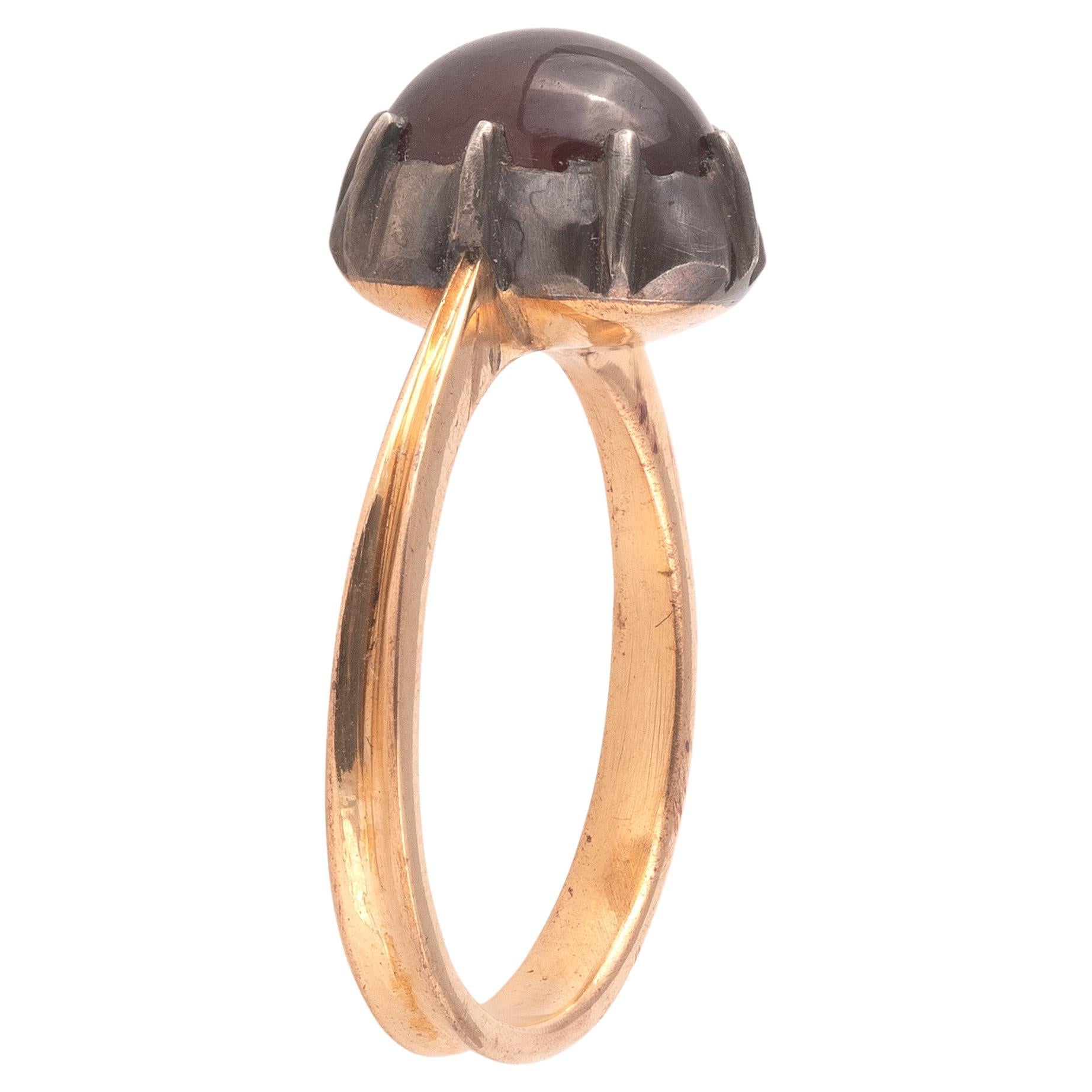 Centering an oval cabochon garnet, handcrafted Georgian style cut-down collet setting of black silver on 18ct yellow gold with a rounded 18ct yellow gold band. 
Size: 7
Weight: 6gr.
