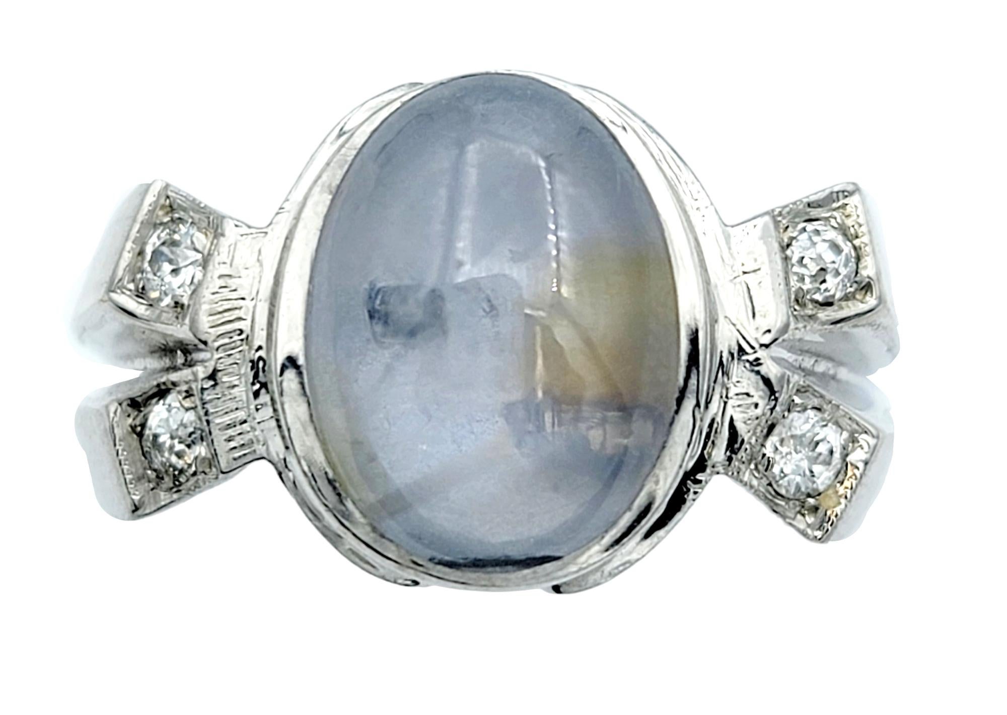 Ring Size: 9.5

This unique 14 karat white gold ring is an elegant piece that exudes timeless charm. At its center lies an oval cabochon star sapphire with a soft, light grayish-blue hue, reminiscent of a tranquil sky. Gracefully adorning the ring