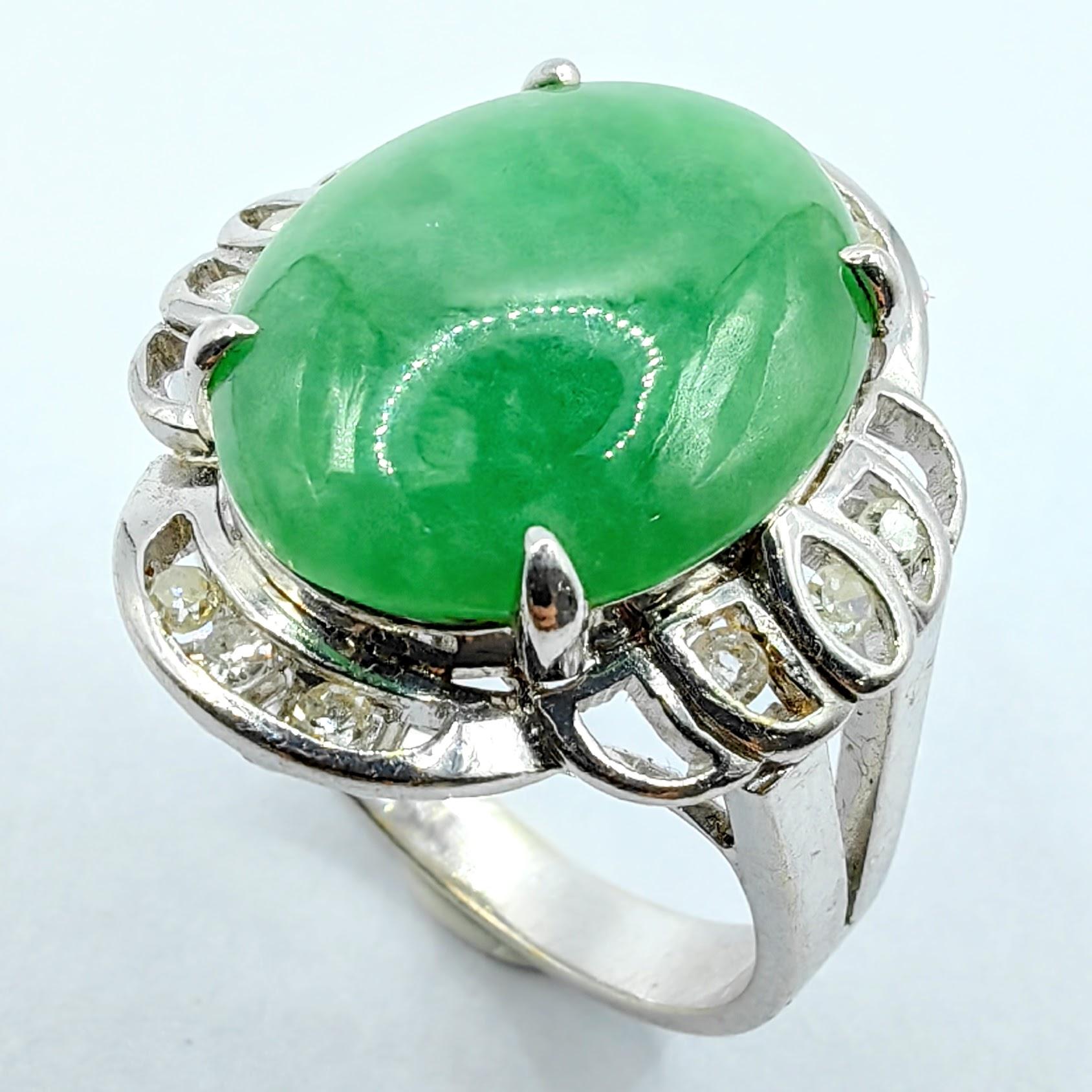 This magnificent ring showcases a substantial oval cabochon of genuine Burmese jadeite in a vibrant apple green hue, framed by an elegant halo of twelve round brilliant cut diamonds set in luxurious 18K white gold. The jade's smooth, polished