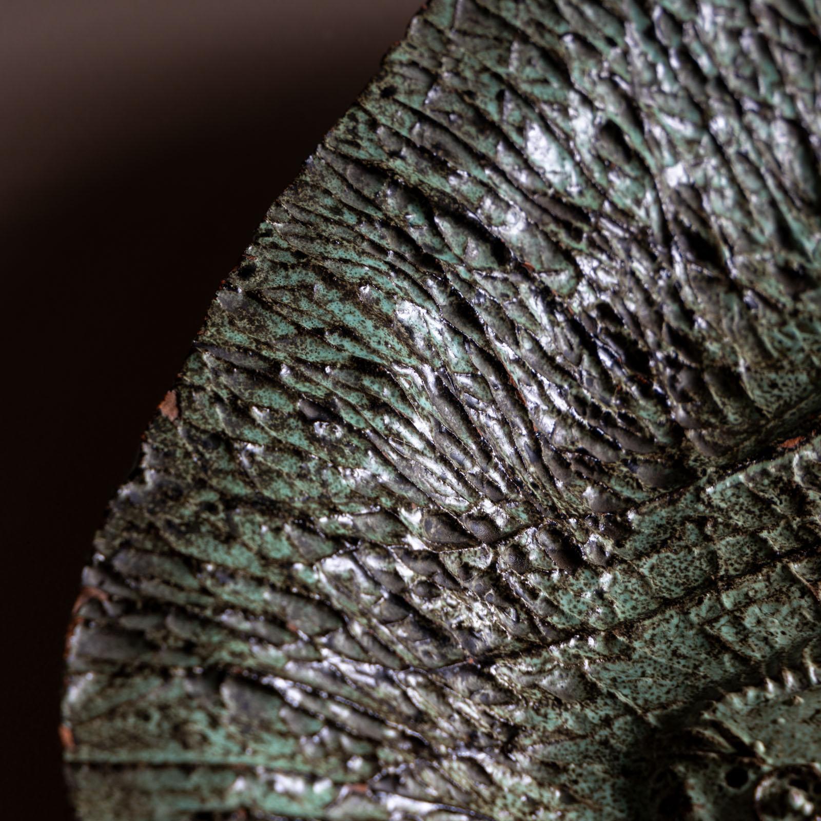 Plato ovalado de cerámica con estilizados peces reflejados sobre un fondo muy texturado. Con una pátina verde-negra y una estructura irregular, este cuenco de cerámica desprende un carácter intrigante y dramático. 