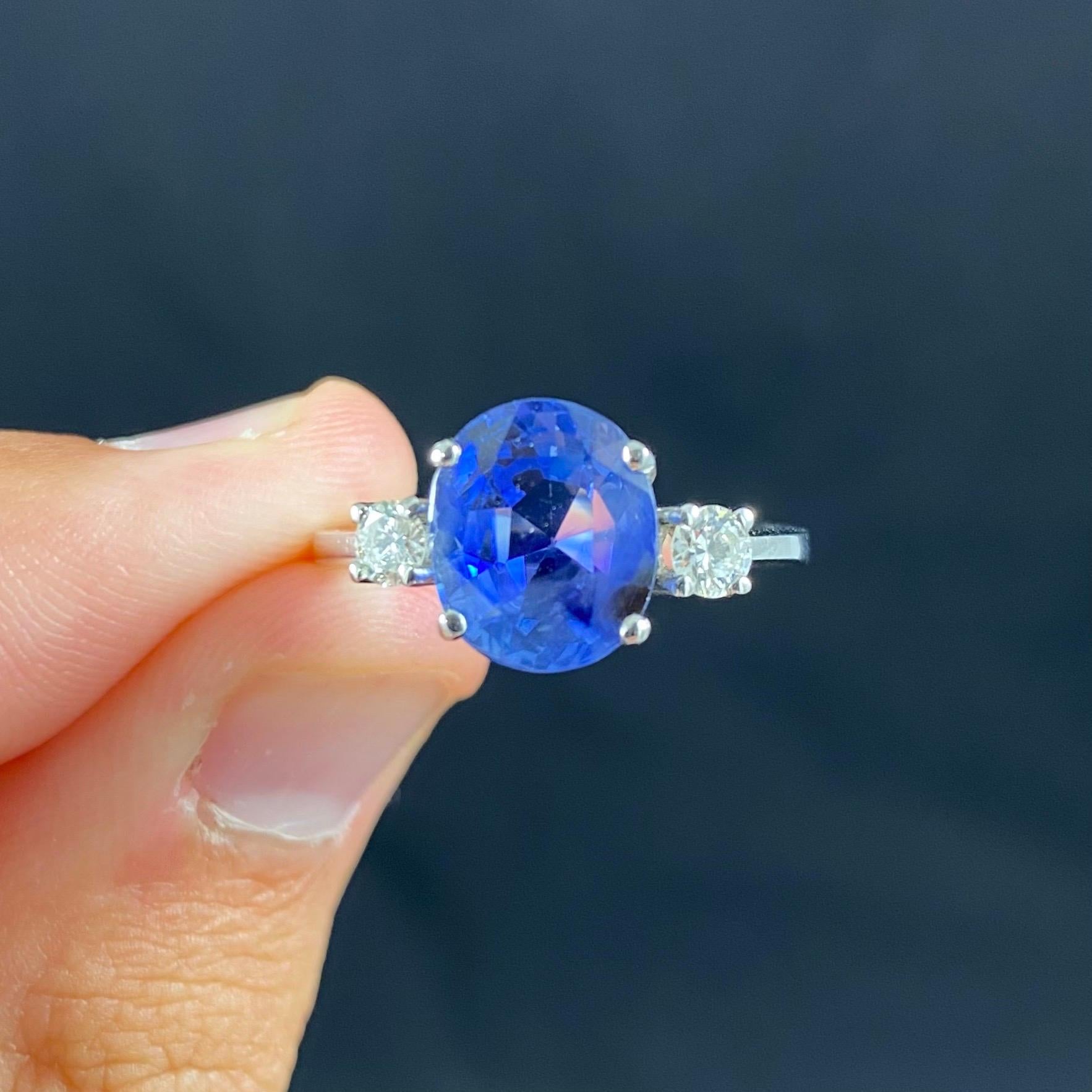 A contemporary oval sapphire and round brilliant-cut diamond three-stone engagement ring in 19.2kt white gold. This ring features an oval mixed-cut color-change sapphire claw-set to the center, flanked to each side by a similarly-set round