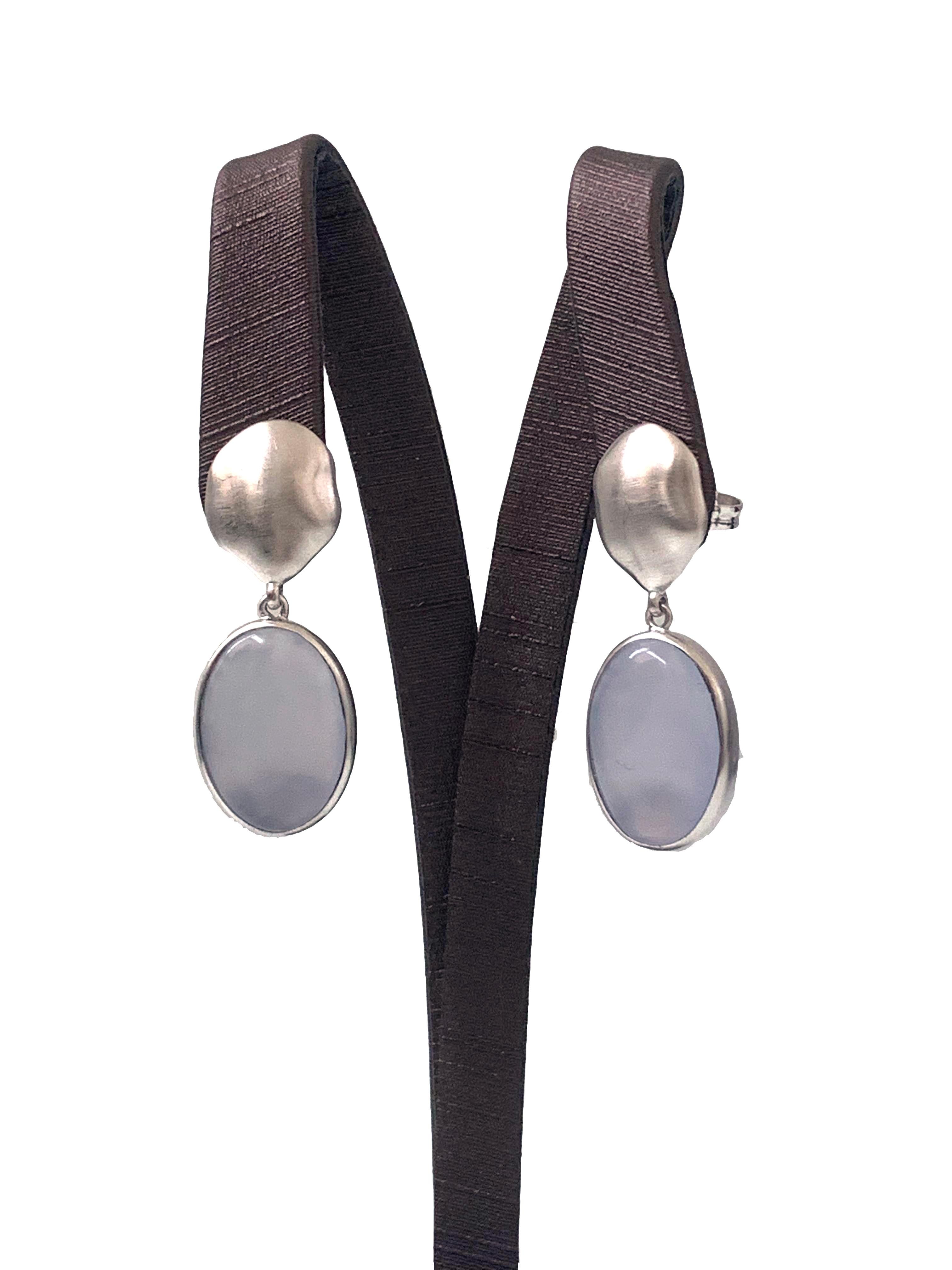 Discover oval Chalcedony drop earrings. The earrings feature 2 large oval-shape cabochon-cut Chalcedony with unique periwinkle purple-ish blue hue, handcrafted brushed satin texturing technique, and hand set in platinum rhodium plated sterling