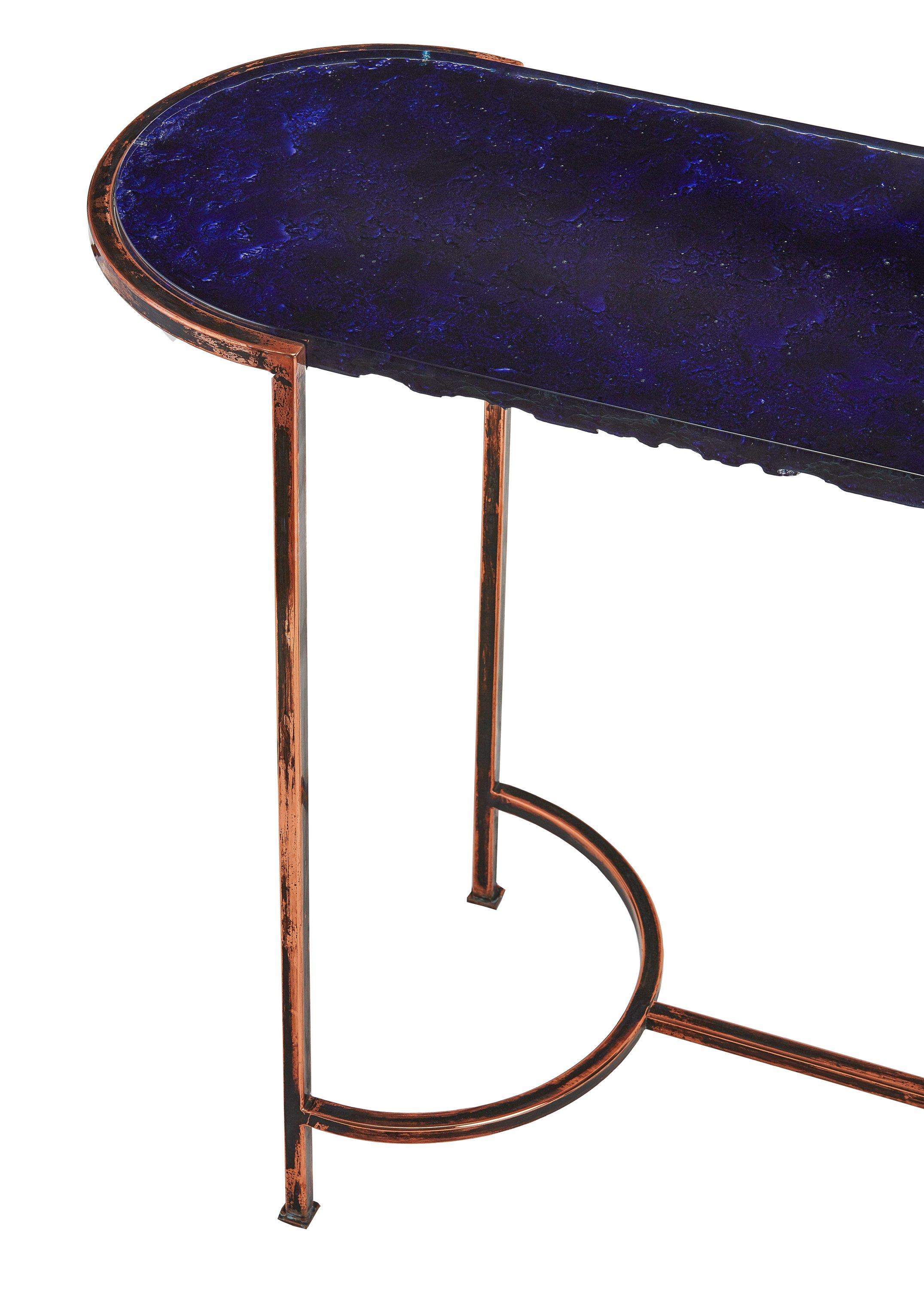 The oval blue glass console with a red copper frame has the shape and image of the eye of the blue mountain lake. The blue cast glass top is 26 mm thick and its backside has silvered irregular wavy texture which looks like moving water. The steel