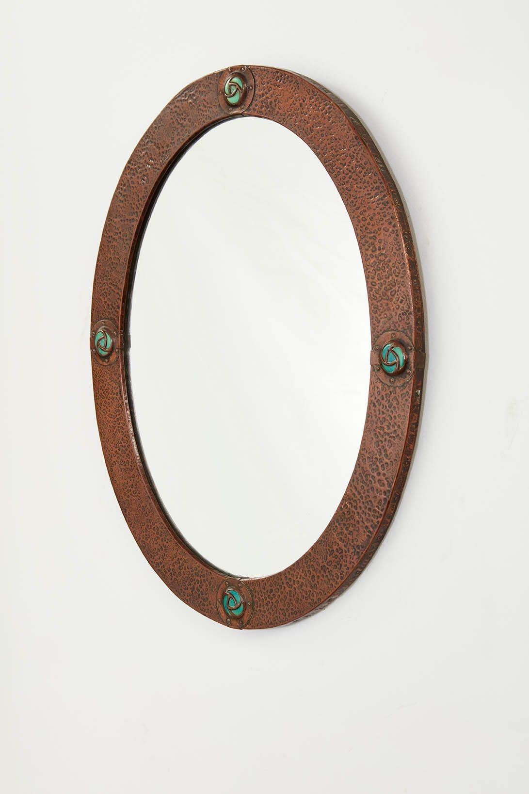 An arts & crafts oval copper mirror with hand hammered frame highlighted by four blue and copper studded cabuchons at the compass points