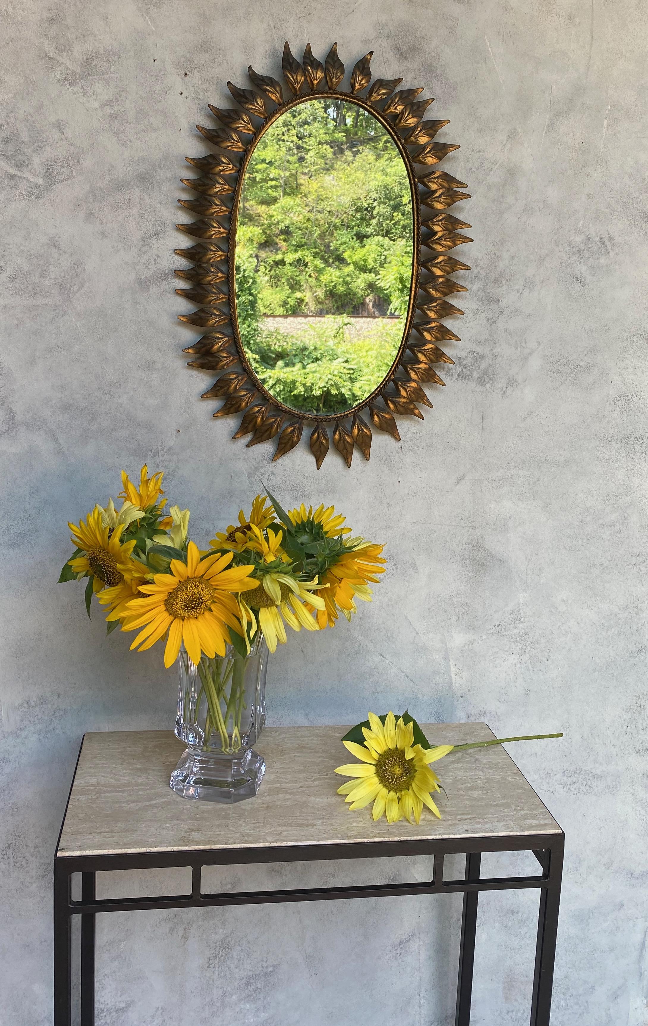 Dieser schöne ovale Spiegel mit Sonnenschliff zeigt geschwungene, strahlenförmige Blätter, die einen Rahmen mit einem zarten Flechtmuster umgeben. Er ist mit einer reichen Goldpatina überzogen. Vor kurzem haben wir den Spiegel mit einer