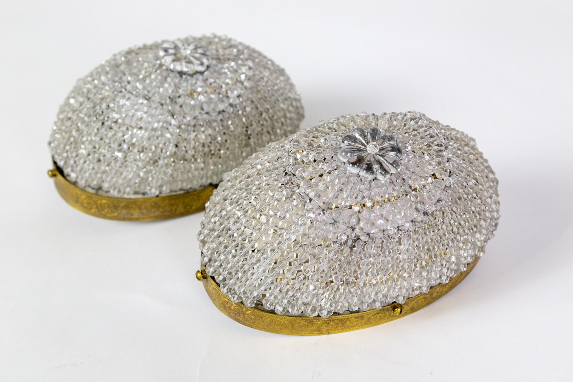 A pair of elliptical basket-style flush mount sconces, that could also be used as ceiling lights, were made circa 1930s.  The oval dome shapes are comprised of crystal bead strands with a rosette crystal at the center.  They are banded with a