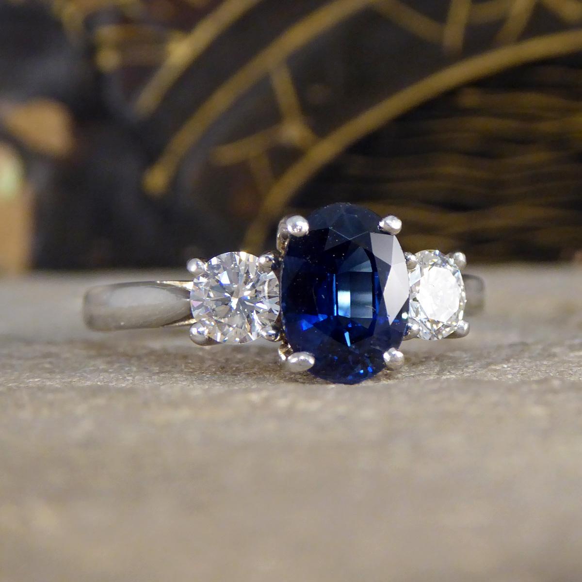 This modern Oval Cut Sapphire and Diamond three stone ring in Platinum showcases contemporary elegance and timeless sophistication. The centre piece of this exquisite design is a stunning 1.75ct oval cut sapphire, known for its deep, enchanting blue