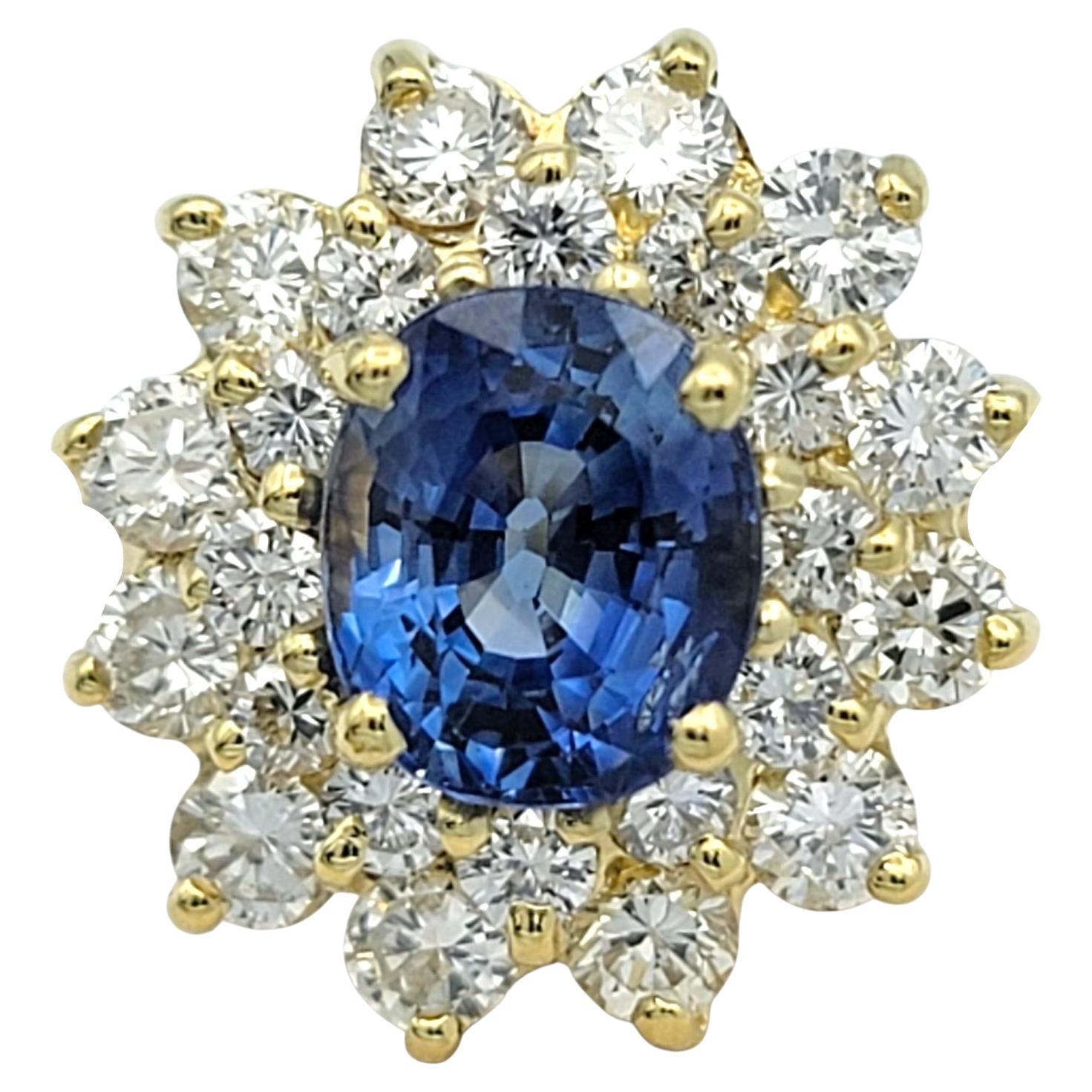 Cette bague en saphir et diamant est réalisée en or jaune 18 carats et met en valeur un saphir bleu de taille ovale en son centre. Le saphir est entouré d'un halo de diamants ronds disposés en étoile qui rehausse la couleur riche et profonde de la