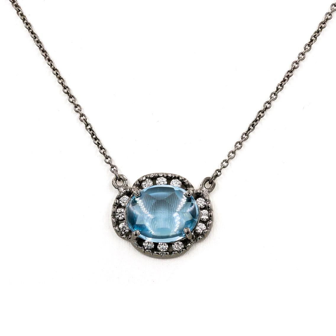 This elegant Lester Lampert original pendant in 18kt. white gold contains an oval cut cabochon blue topaz center= 2.60cts. that is surrounded by 12 ideal cut round diamonds approximately=.25ct. t.w. The round diamonds are G in color and VS in