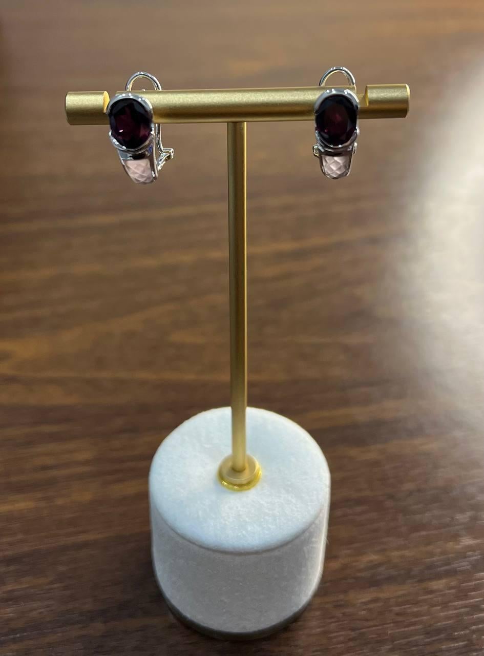 A striking pair of earrings.

These elegant earrings feature a deep red oval garnet set in a sleek white gold mounting. The gemstones are faceted, enhancing their rich color and brilliance. The design is both modern and timeless, with a smooth,