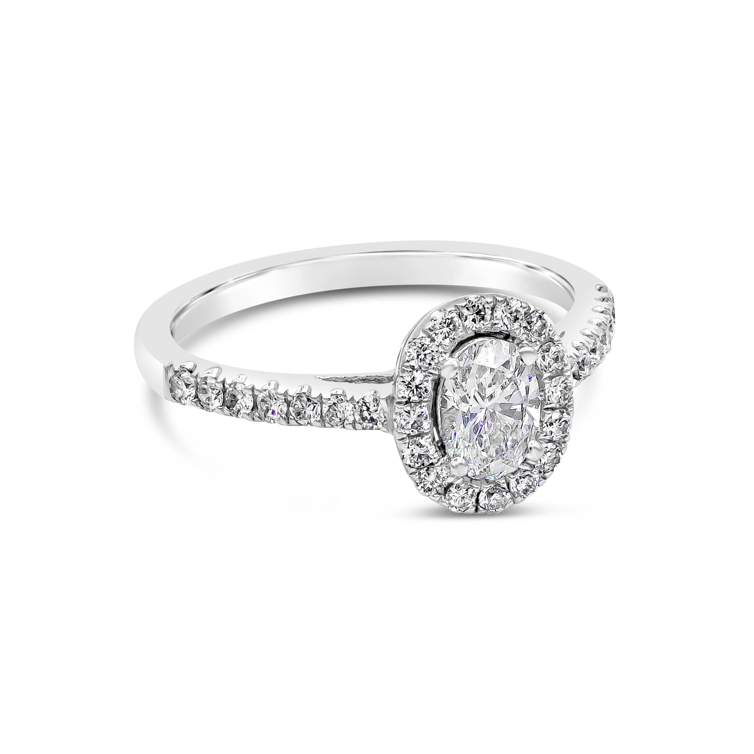 A simple and modern engagement ring design showcasing a 0.53 carats oval cut diamond, set in a classic four prong basket setting. Surrounded by a row of round brilliant diamonds in halo pave setting. Shank is diamond encrusted in half eternity