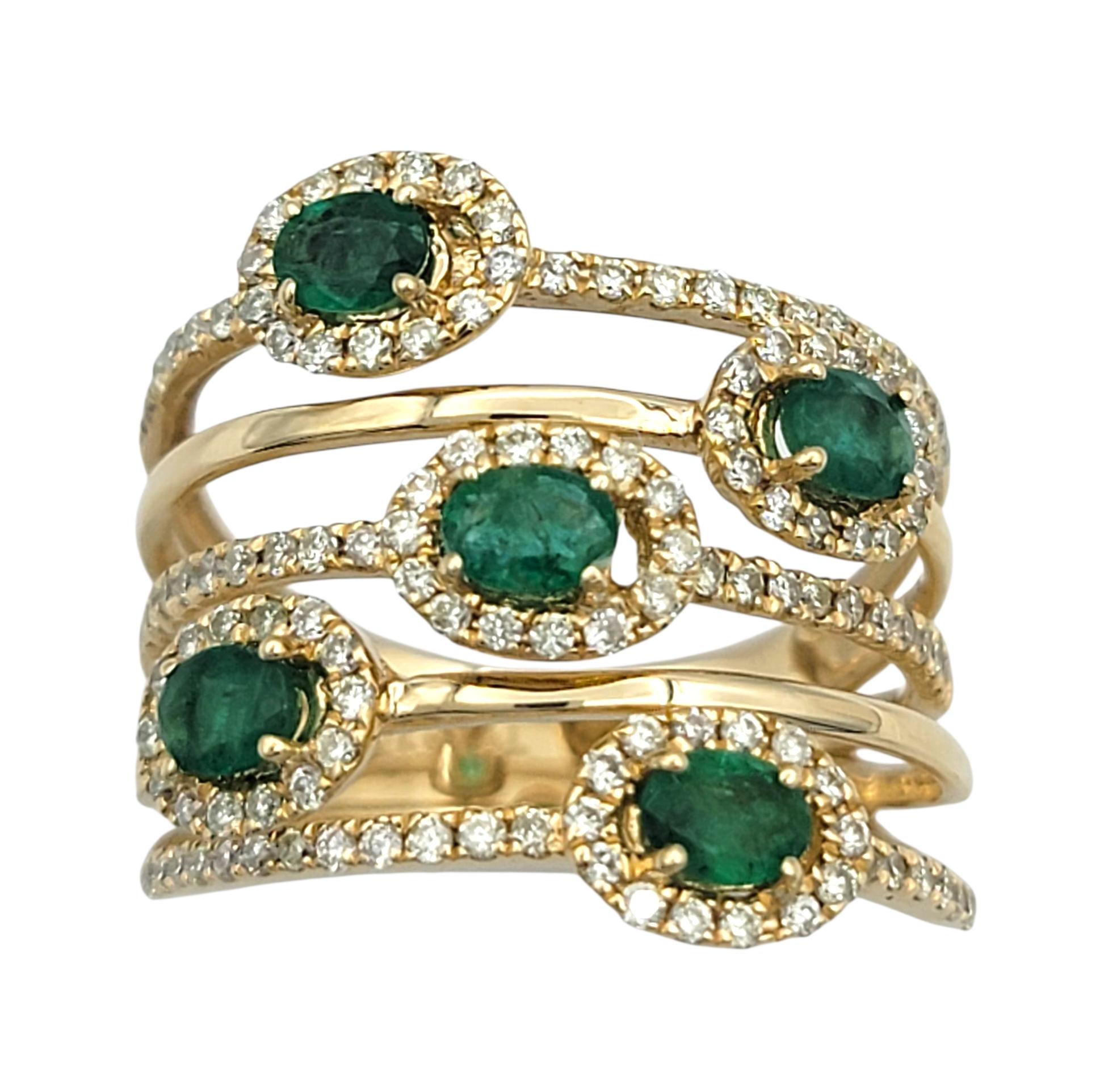 Cette bague en or jaune 14 carats présente un motif captivant à plusieurs rangs, serti de cinq émeraudes naturelles de taille ovale. Chaque émeraude d'un vert éclatant est entourée d'un halo de diamants étincelants, rehaussant sa riche couleur et