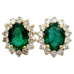 Oval Cut Emerald and Diamond Halo Stud Earrings in Polished 14 Karat Yellow Gold