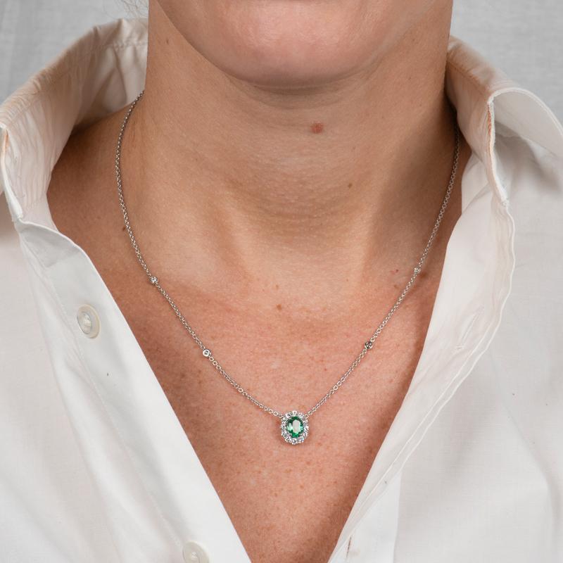 This 18 karat white gold necklace features a 0.68 carat oval cut natural emerald accented by 0.48 carat total weight in round diamonds on a diamonds by the yard style chain. Lobster clasp closure. Wear alone or layer with your other favorite
