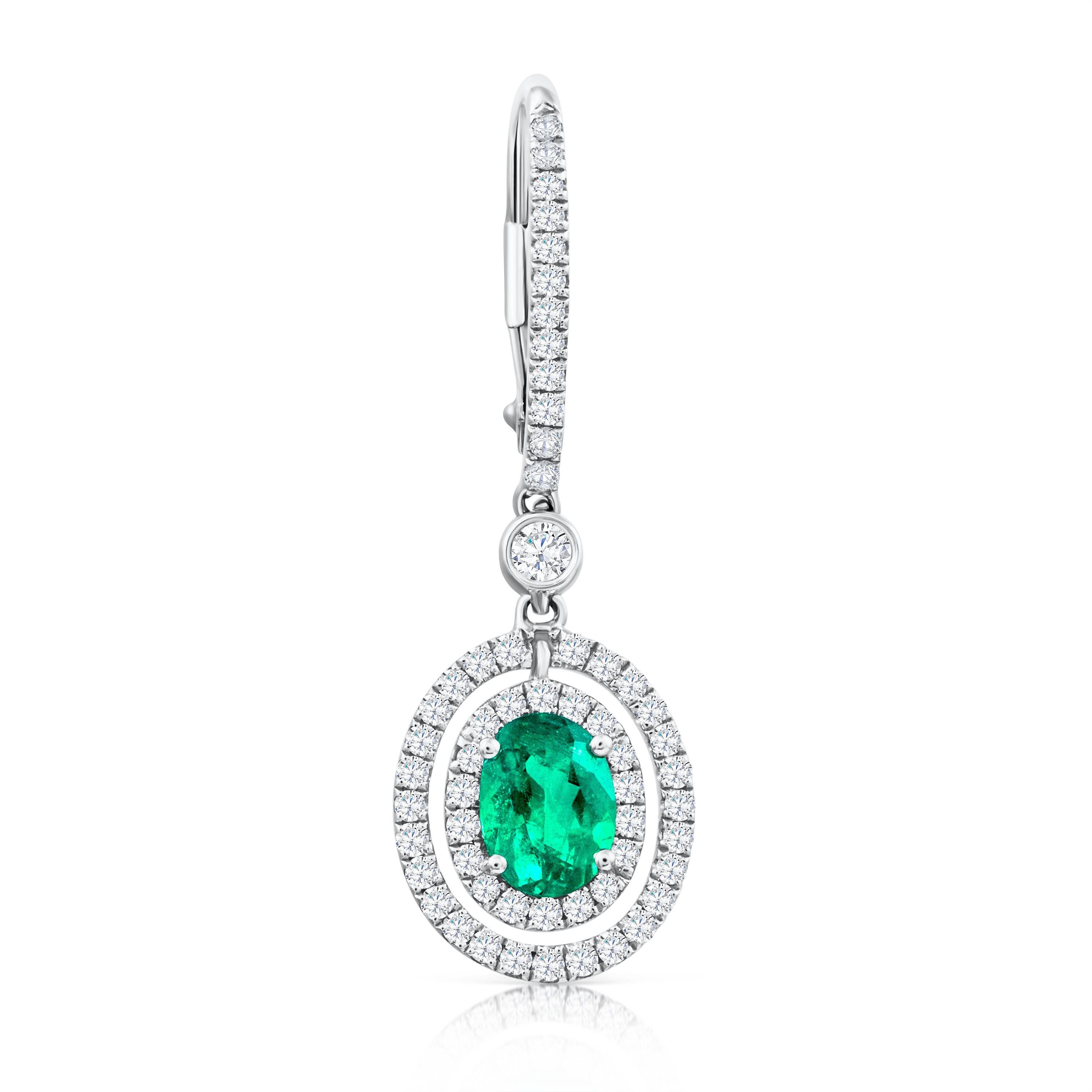 Simple but elegant 18k white gold dangle earrings set with 2 oval cut green emeralds weighing 1.01 carats total. The emeralds are surrounded by 2 rows of brilliant round diamonds weighing 0.63 carats suspended on an accented lever-back. Spaced by a
