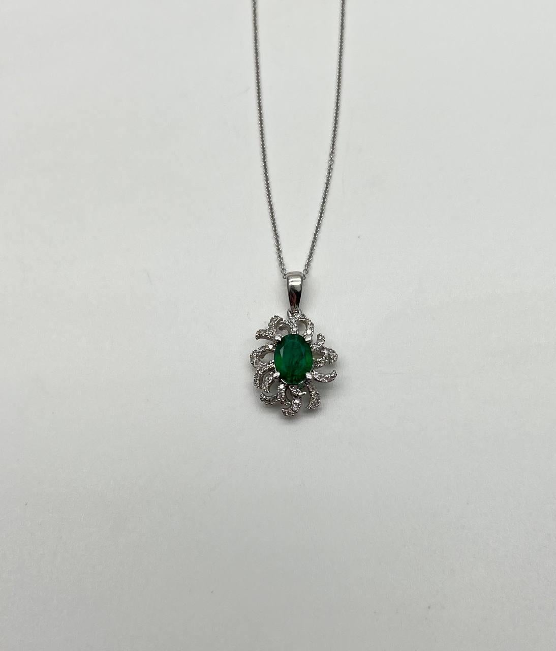 A stunning pendant necklace, this exquisite piece features a vibrant green oval emerald at its center.
The gemstone is elegantly surrounded by a series of intricate, swirling designs encrusted with sparkling diamonds, creating a captivating floral