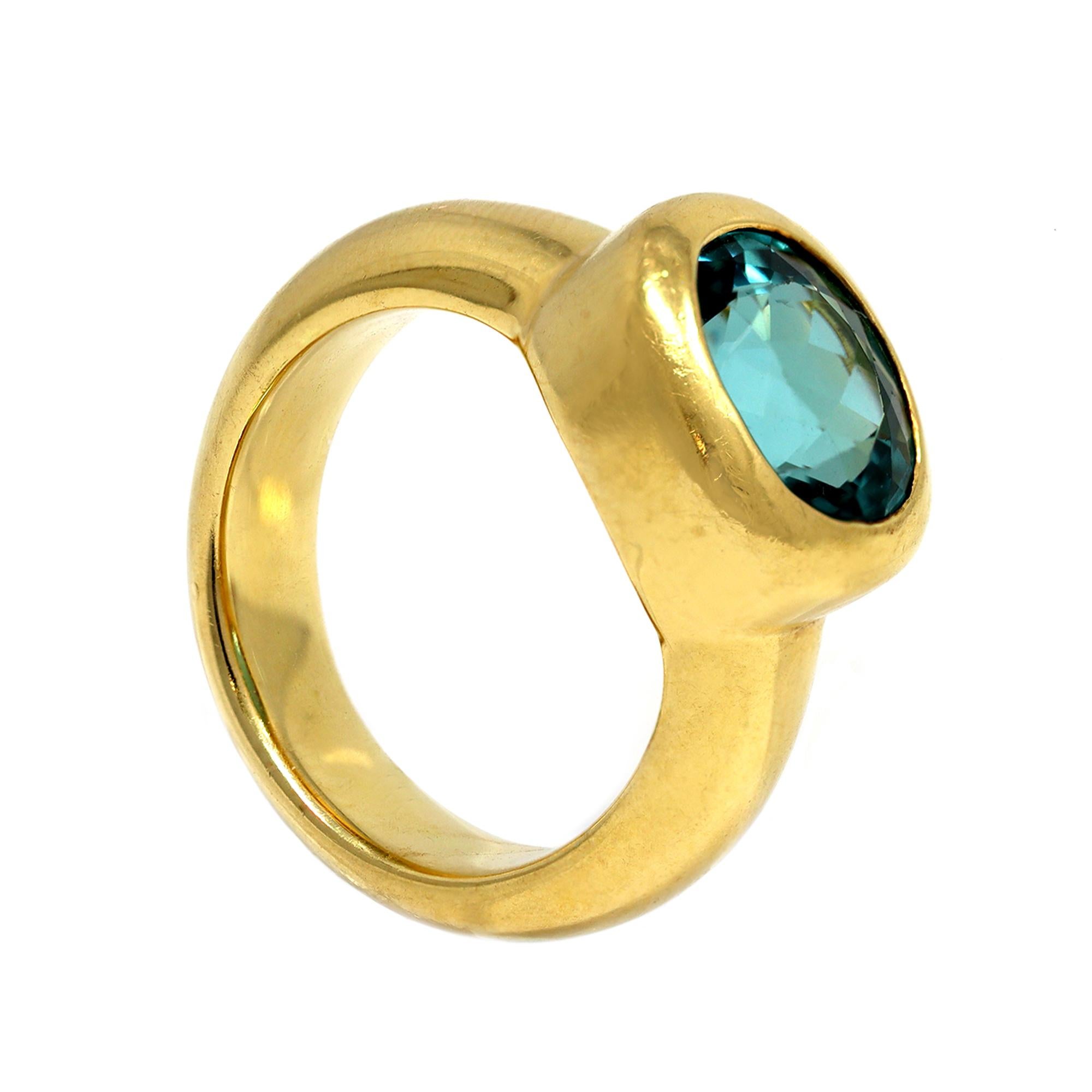 The oval faceted shape tourmaline displays a uncommon light blueish green color, with very clean crystal quality. The stone is set in a heavy bezel and larger band in 18 karat yellow gold. The hand made ring is 0.43” wide and fits a size 6 ¼. The