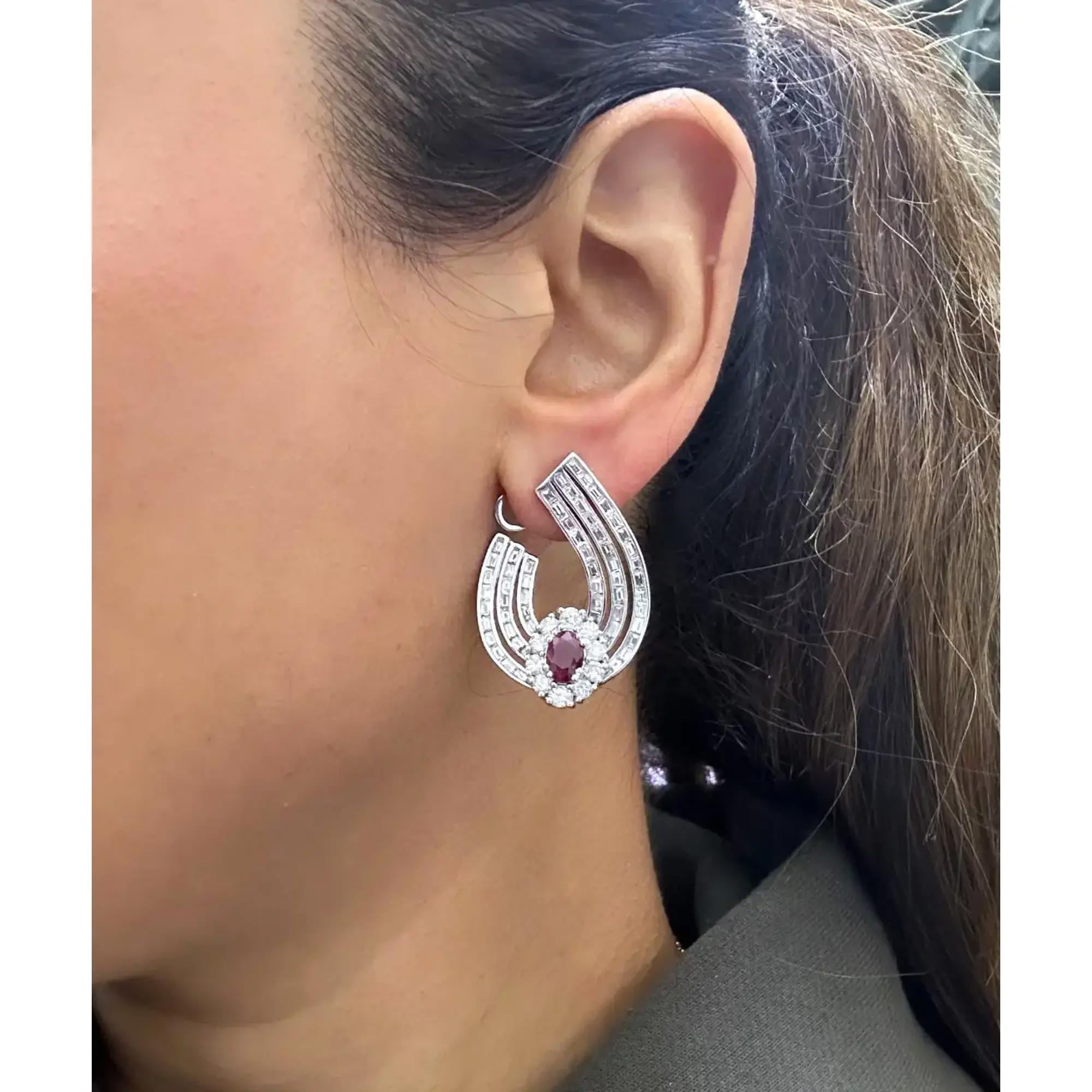Elevate any attire with these dazzling earrings crafted in fine 14K white gold. These earrings feature a center prong set oval cut ruby with channel set baguette cut and prong set round cut diamonds encrusted in a half hoop style. Total ruby weight: