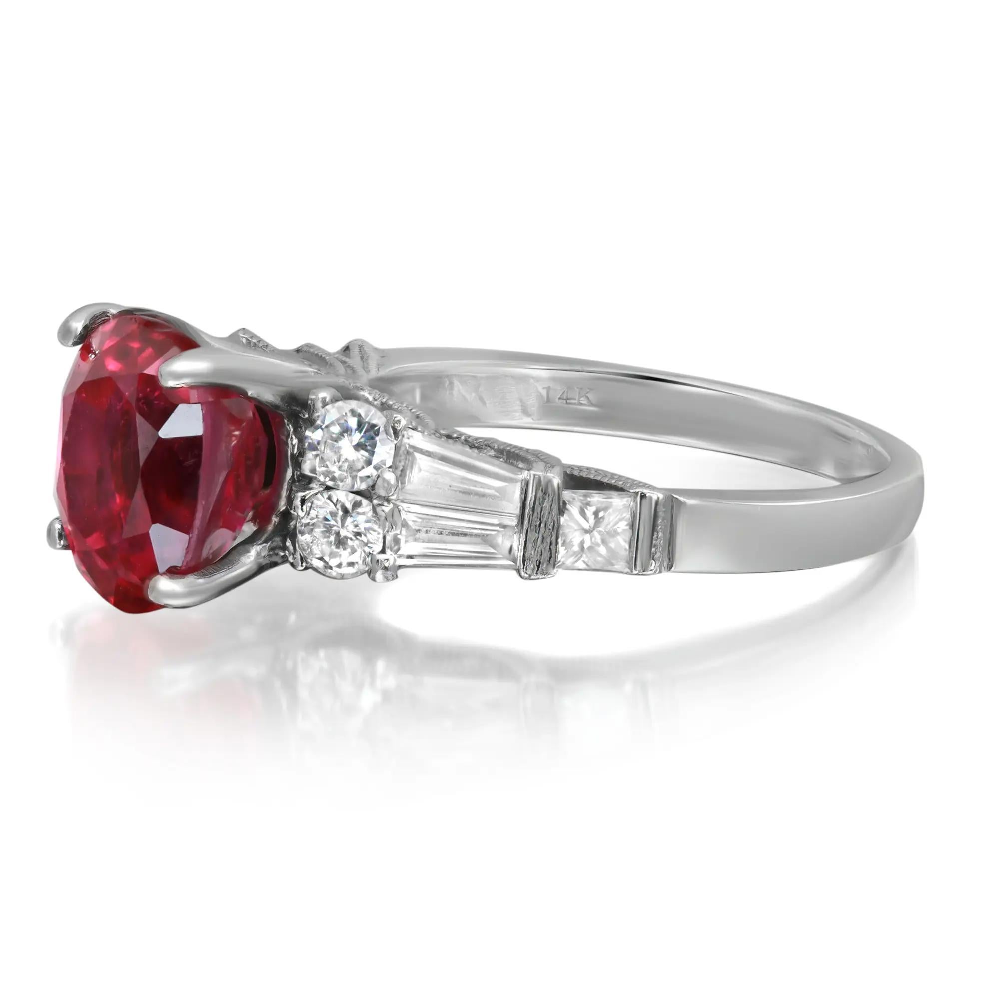 This beautiful Ruby and diamond cocktail ring is crafted in lustrous 14k white gold, it features a center prong set oval cut pinkish red ruby with round, baguette and princess cut diamonds on each side. The ruby is clarity enhanced and lead glass