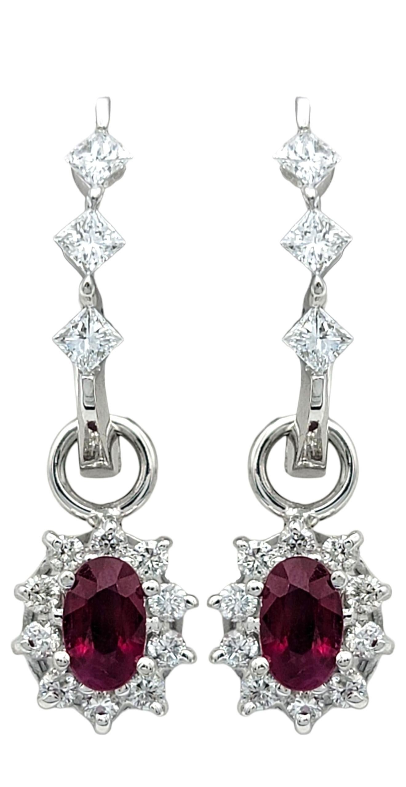 These elegant ruby and diamond earrings offer both beauty and versatility. Crafted in 14 karat white gold, each earring features a vivid oval ruby surrounded by a sparkling halo of diamonds, suspended from a diamond-set hoop. The ruby dangles can be