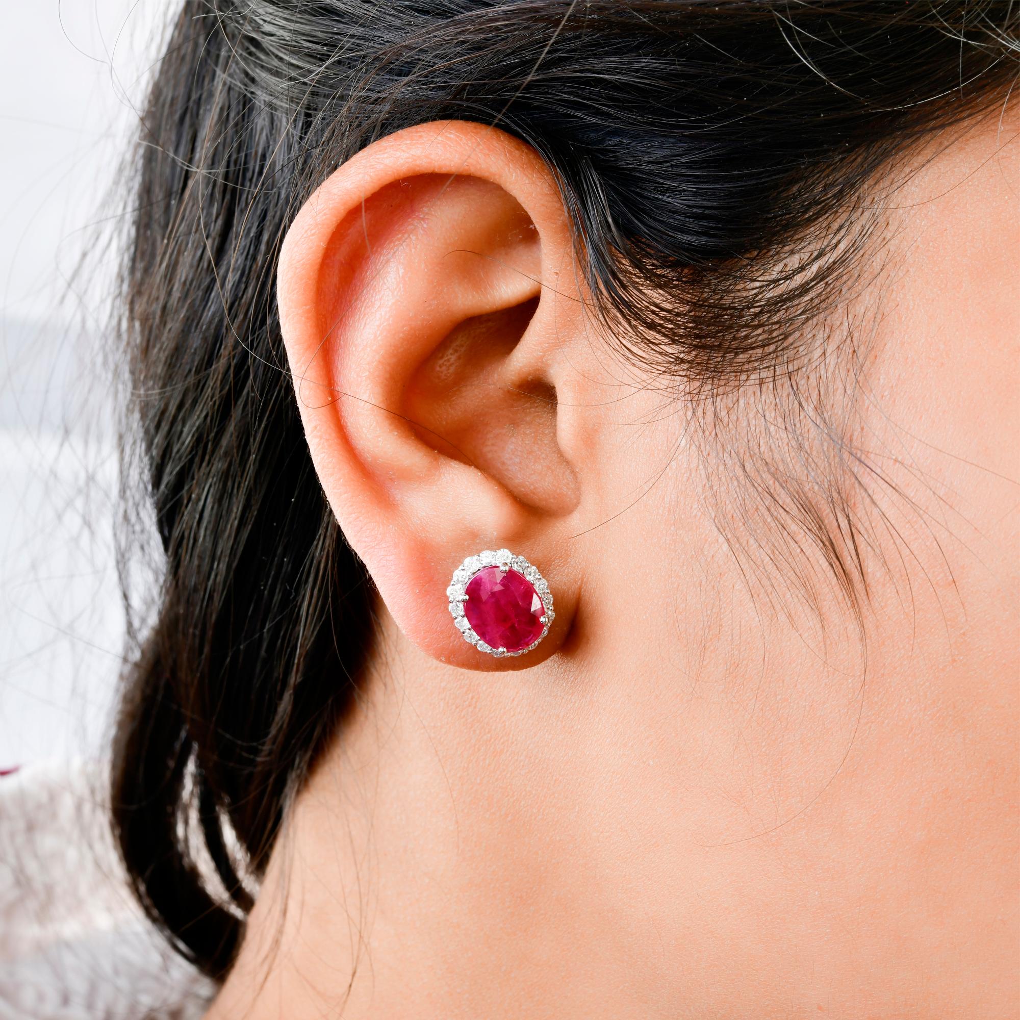 Ces boucles d'oreilles en or blanc 14 carats sont composées d'un rubis de taille ovale au centre et de diamants entourant la pierre. 
Les rubis symbolisent la passion, la confiance et la prospérité. C'est une pierre de naissance du mois de juillet