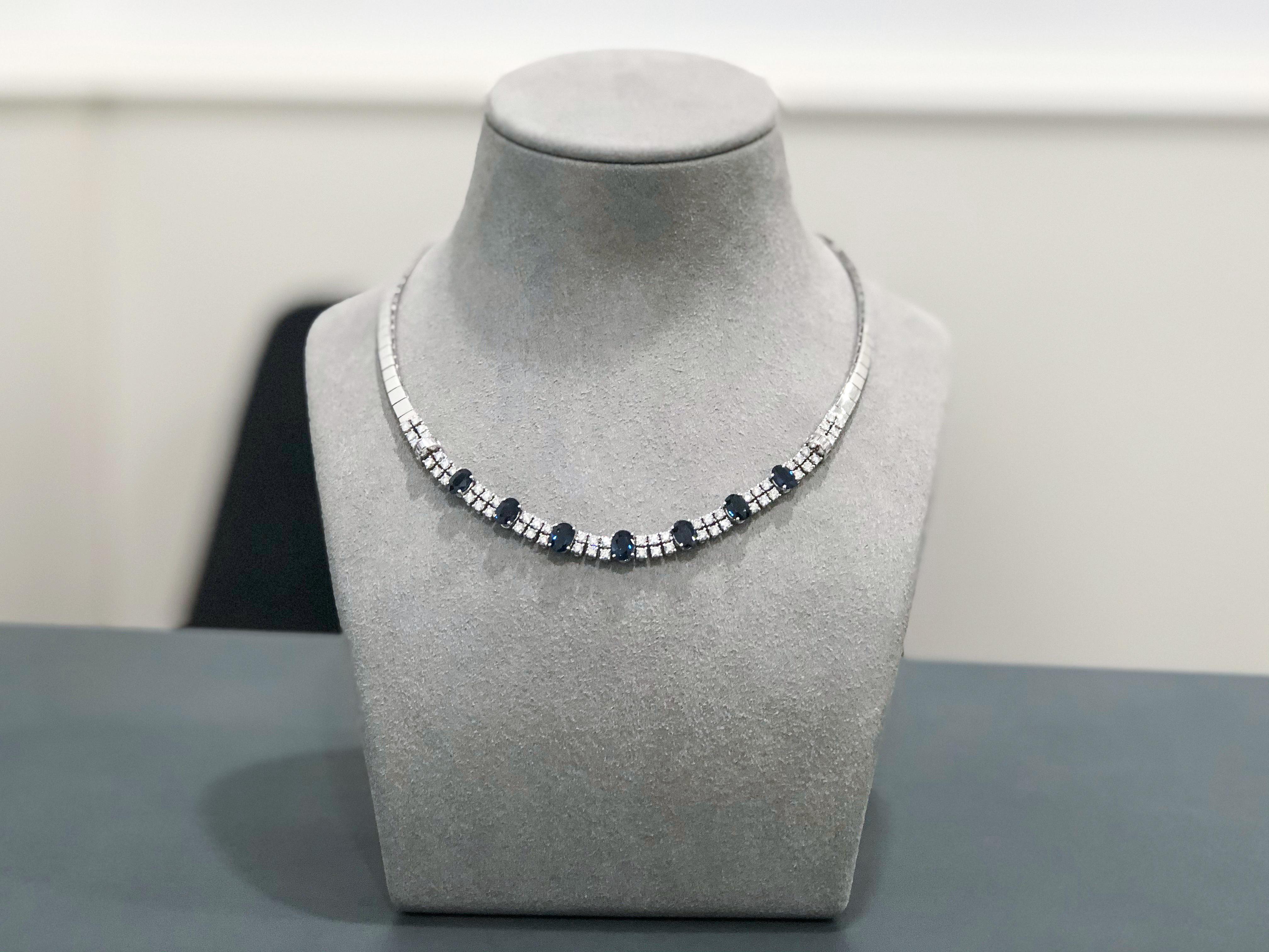 Fashionable necklace set with 7 natural blue sapphires. Each sapphire spaced with 2 rows of round brilliant diamonds. Baguette diamonds channel set in a circular design attached on each side of the necklace. A timeless piece. Set in 18k white