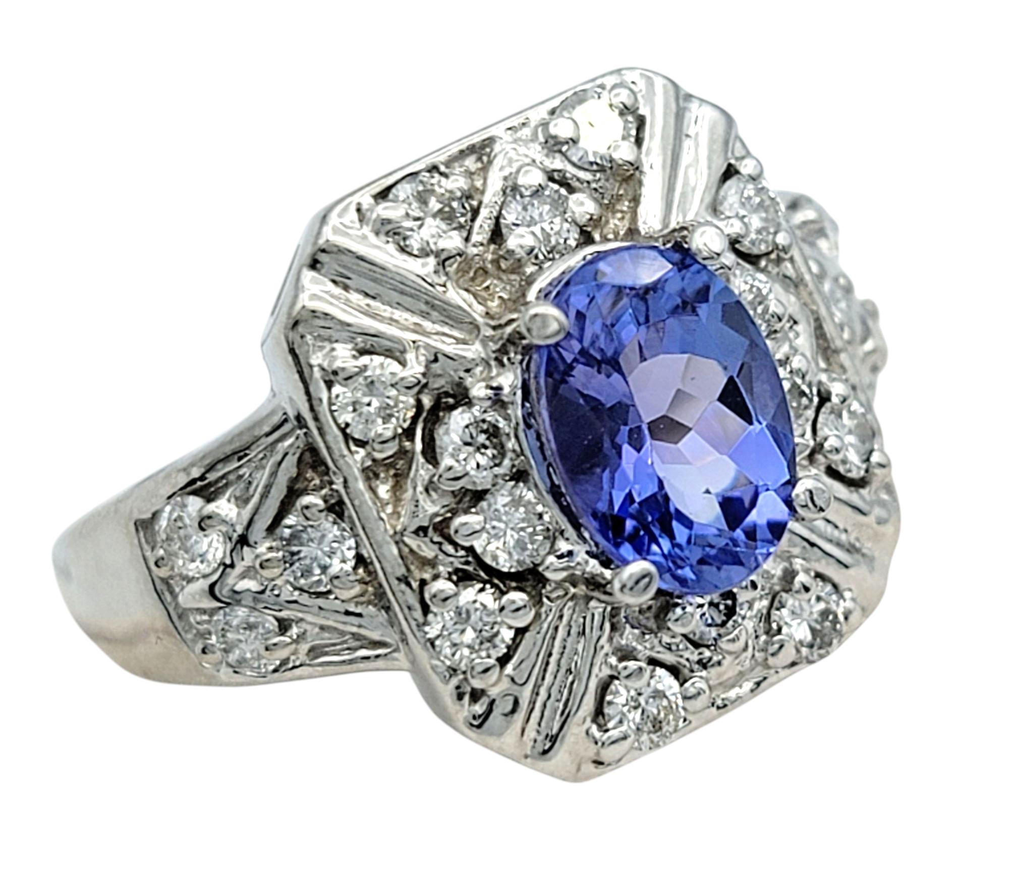 Ring Size: 7

Bold and romantic, this ornate tanzanite and diamond ring is a true statement piece. At the center is a stunning oval-shaped tanzanite in a grayish violet hue, glowing beautifully against its 14 karat white gold setting. The eye-clean