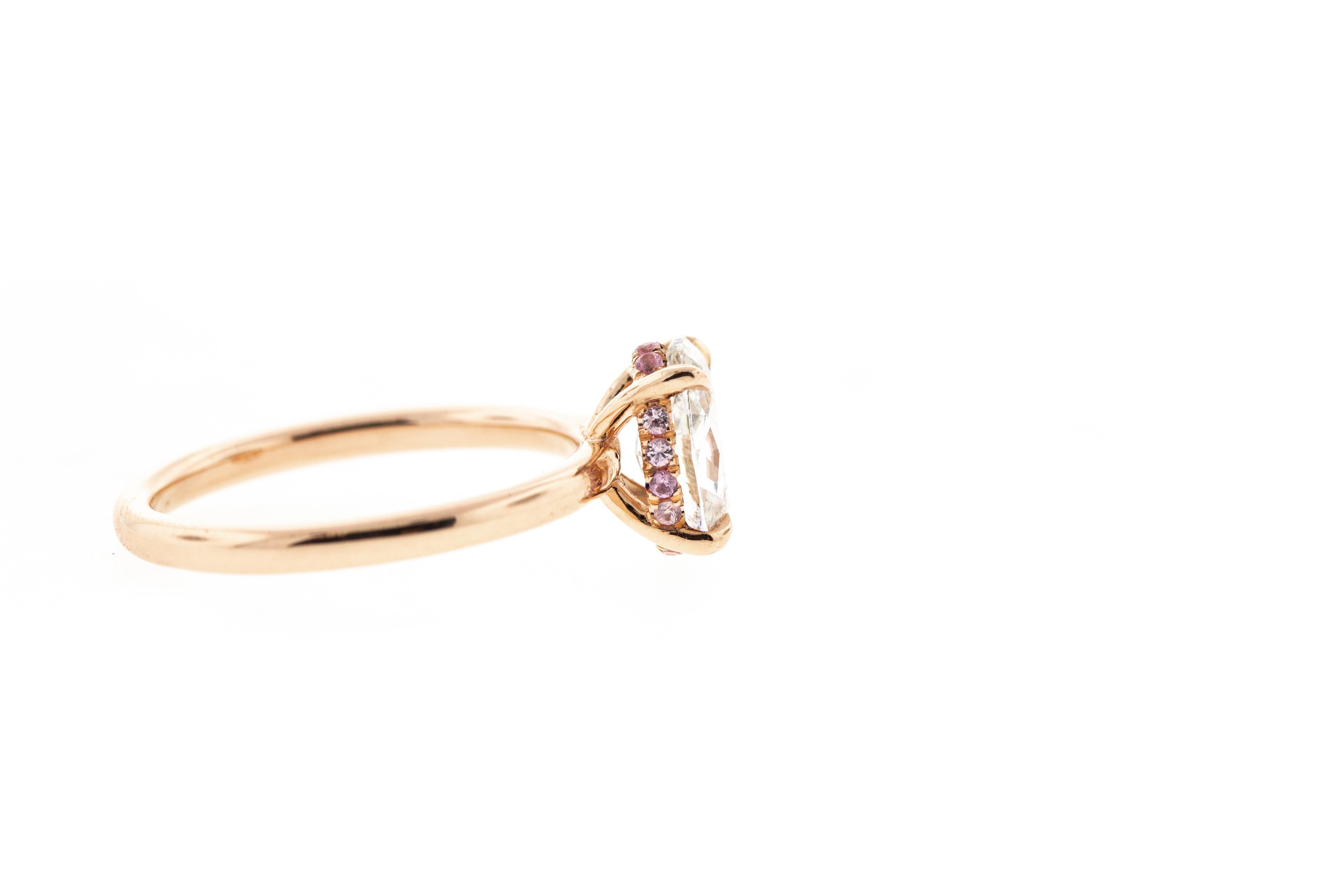 This rose gold engagement ring features an oval diamond for its center stone. A head-on shank setting with a hidden halo of pink sapphires encircles the center diamond. Made in rose gold, this ring can be customized in any color metal. 
