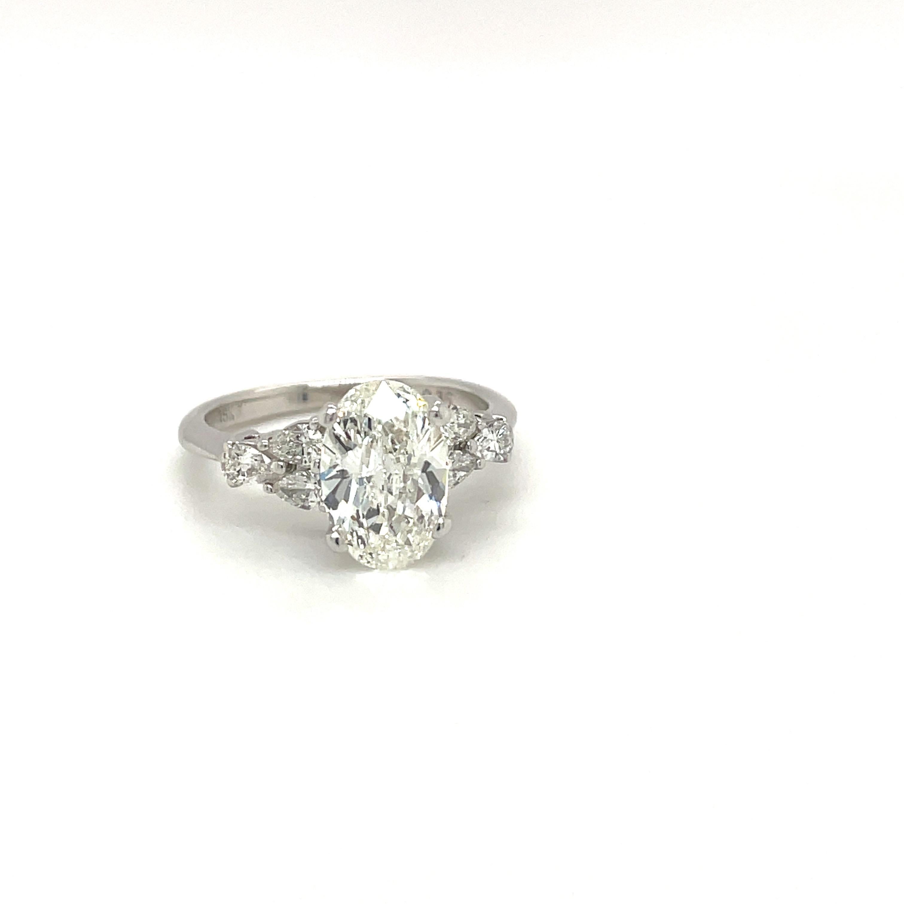 Beautiful oval diamond center stone ring. The GIA certified oval diamond weighs 1.71 carats , H color VS1 in clarity. The center stone is mounted in a platinum setting with 6 pear shaped 0.35 carats diamonds ,3 on each side that form a triangular