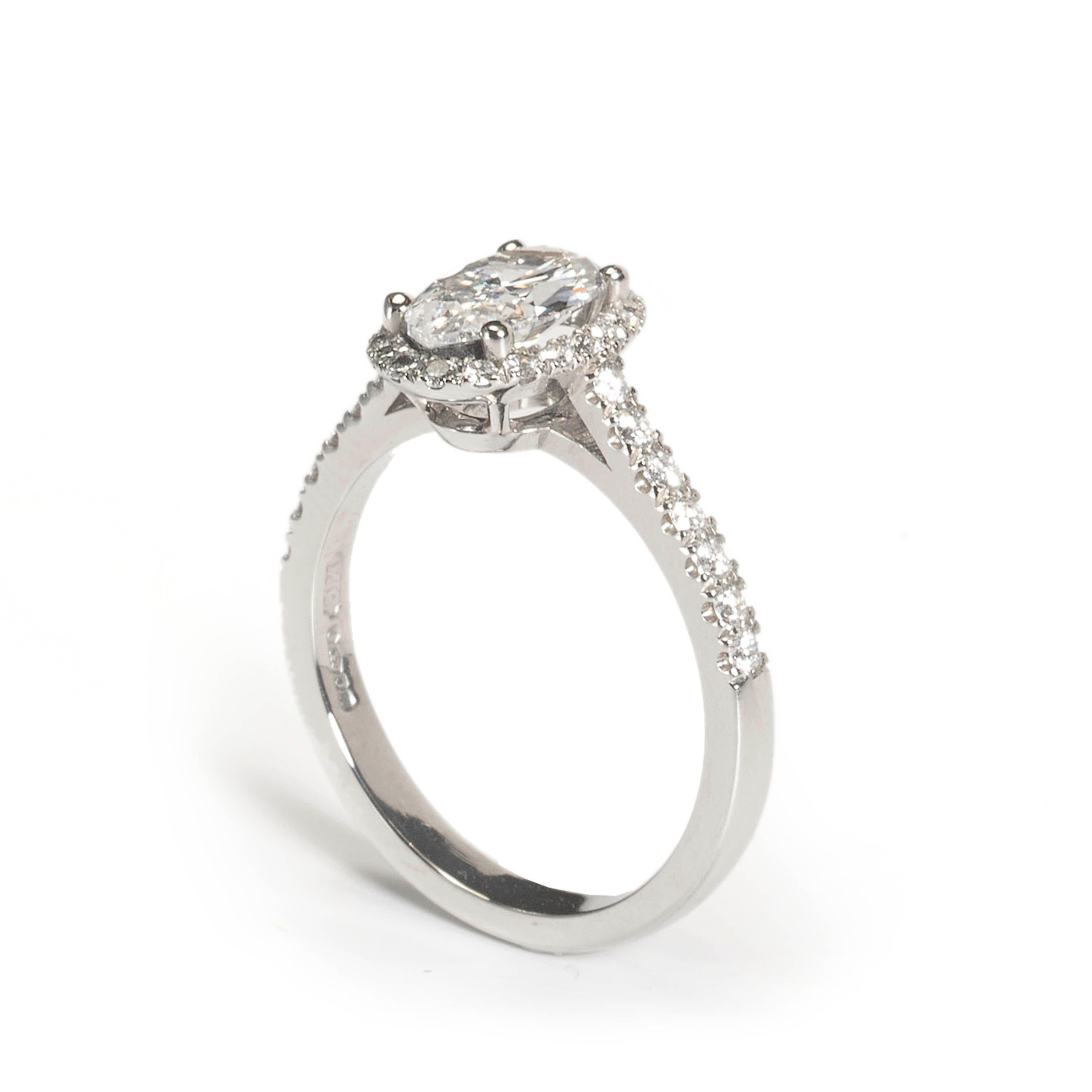A micro pavé halo ring, set with a 1.00ct, D colour, VS2 clarity oval brilliant-cut diamond, in a four claw floating setting, surrounded by a cluster of micro pavé set brilliant-cut diamonds, with a row of seven diamonds, micro pavé set in each