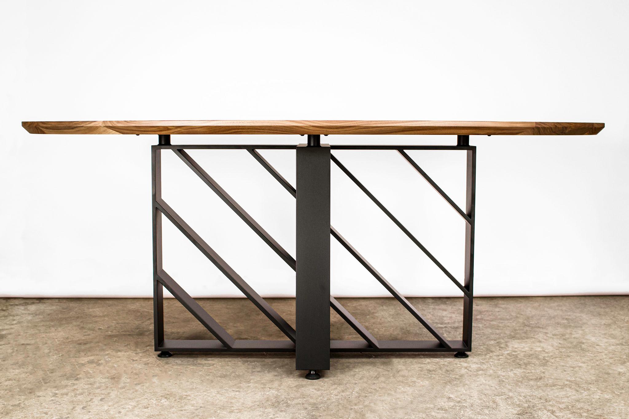 Cette table ovale moderne en acier noirci et en bois dur semble différente sous tous les angles grâce aux mouvements d'ombre et de lumière des plans d'acier. Fabriqué à partir de noyer noir américain et d'une plaque d'acier laminée à chaud de 1/2