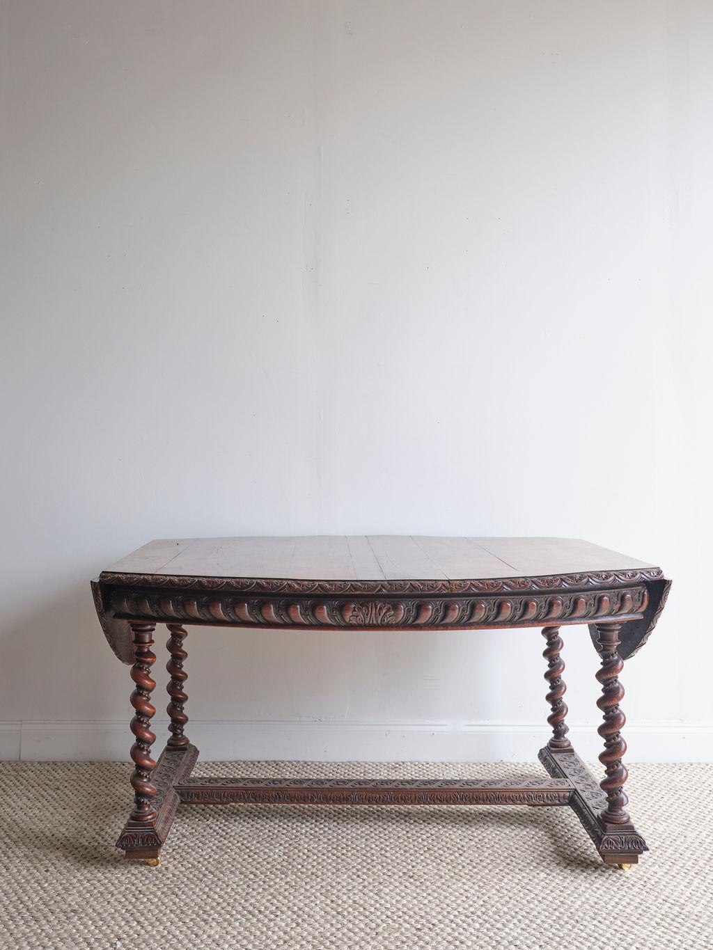 This lovely dark oak oval dining room table is a show stopper piece.. There are two drop-leaf ends to the table and four tuned legs that rest on the table base. There are wood carved details along the side of this table.