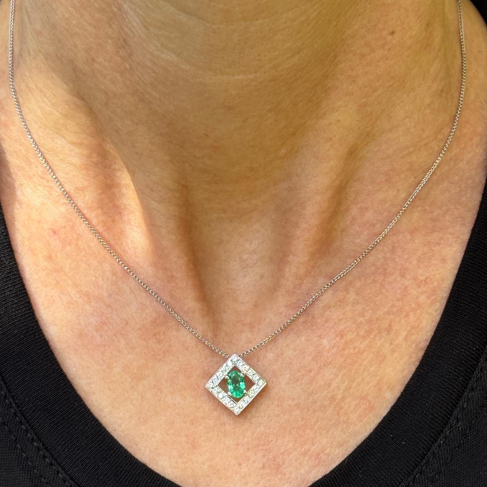 This elegant 14k white gold pendant features a captivating oval emerald of approximately 0.60 carats at its center, celebrated for its vivid green hue. Surrounding the emerald are 20 round brilliant-cut diamonds, totaling approximately 0.25 carats,