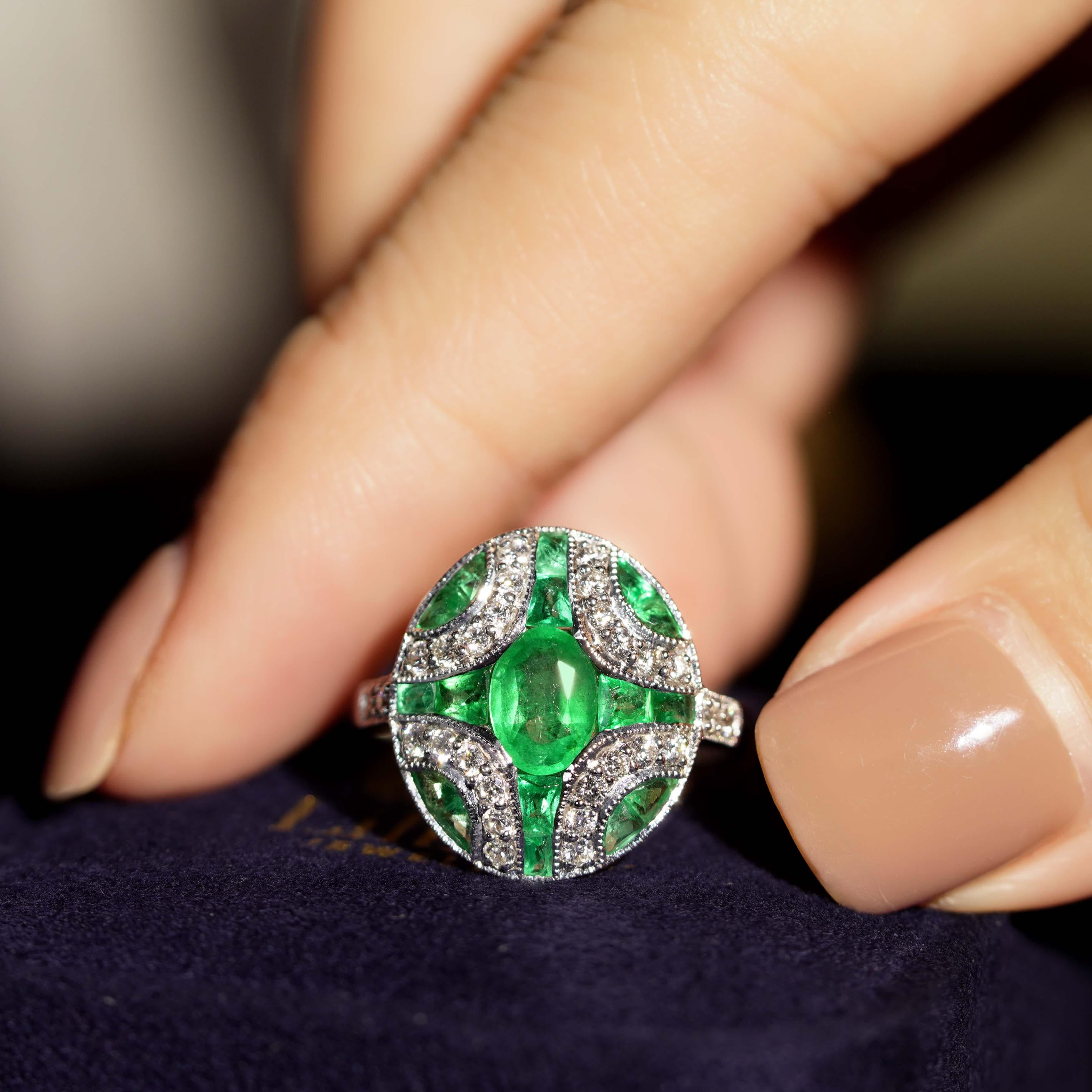 An attractive Art Deco style emerald and diamond ring in milgrain setting centered by an approximately 1.00 carat oval cut emerald adorned by additional French cut emerald flanked by round brilliant diamond line on each corner. This ring, crafted in