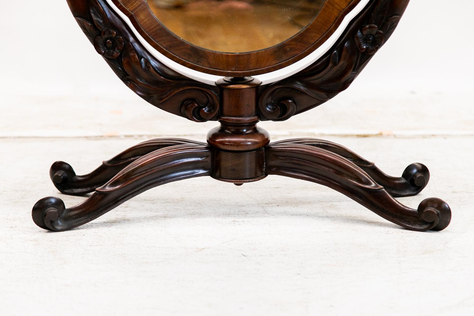 La cornice di questo specchio da toeletta ovale in palissandro inglese è incorniciata da una fascia di mogano a fiamma incrociata. La cornice di supporto è intagliata ad alto rilievo con fiori e foglie. Le quattro gambe sono intagliate nella parte