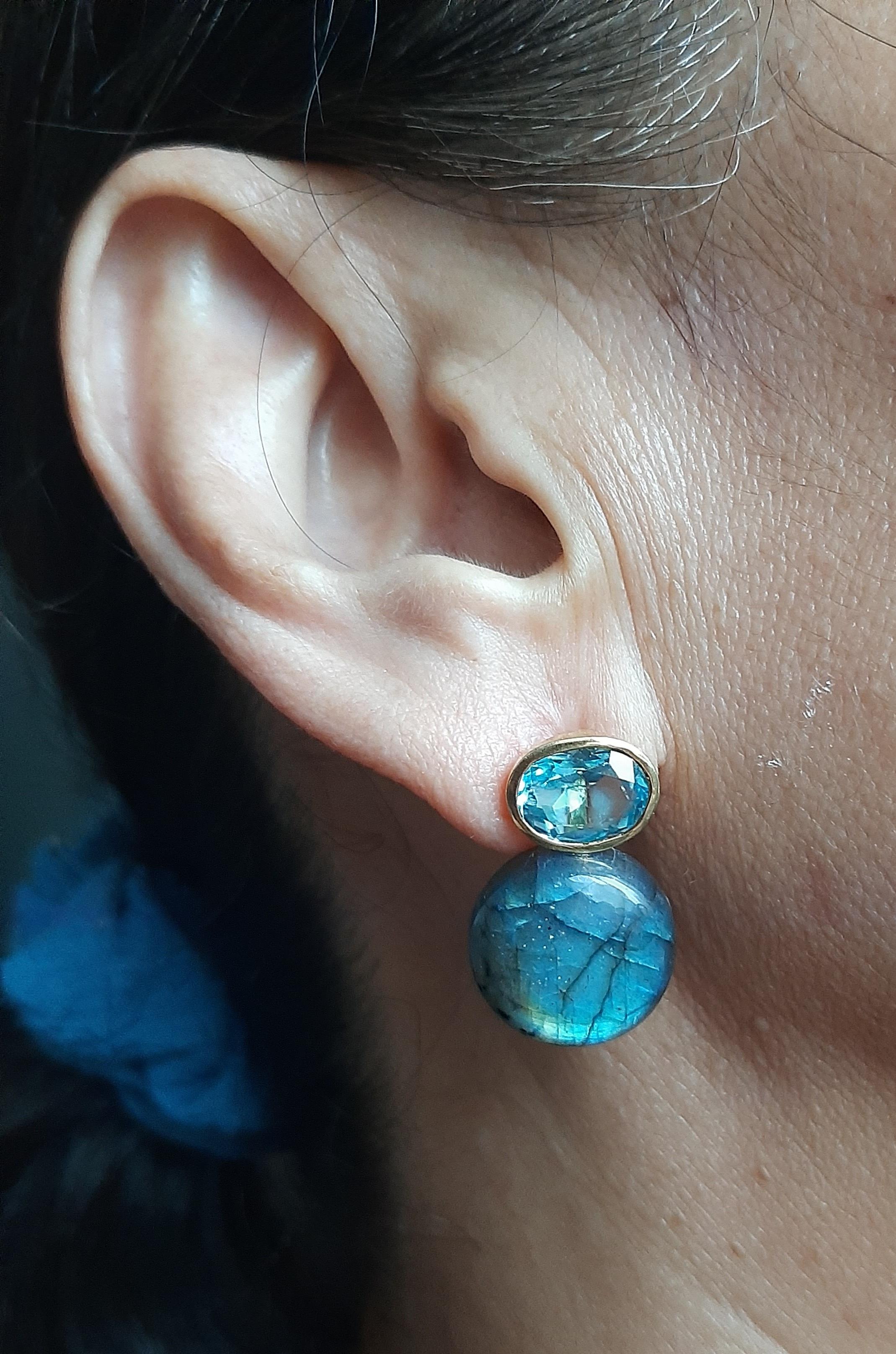 Questi orecchini, semplici ma eleganti e completamente fatti a mano, hanno 2 Topazi Azzurri ovali sfaccettati di 8x 10 mm incastonati in un castone d'oro giallo 14 Kt alla cui sommità sono sospesi 2 bottoni tondi semplici di Labradorite.  17 mm di