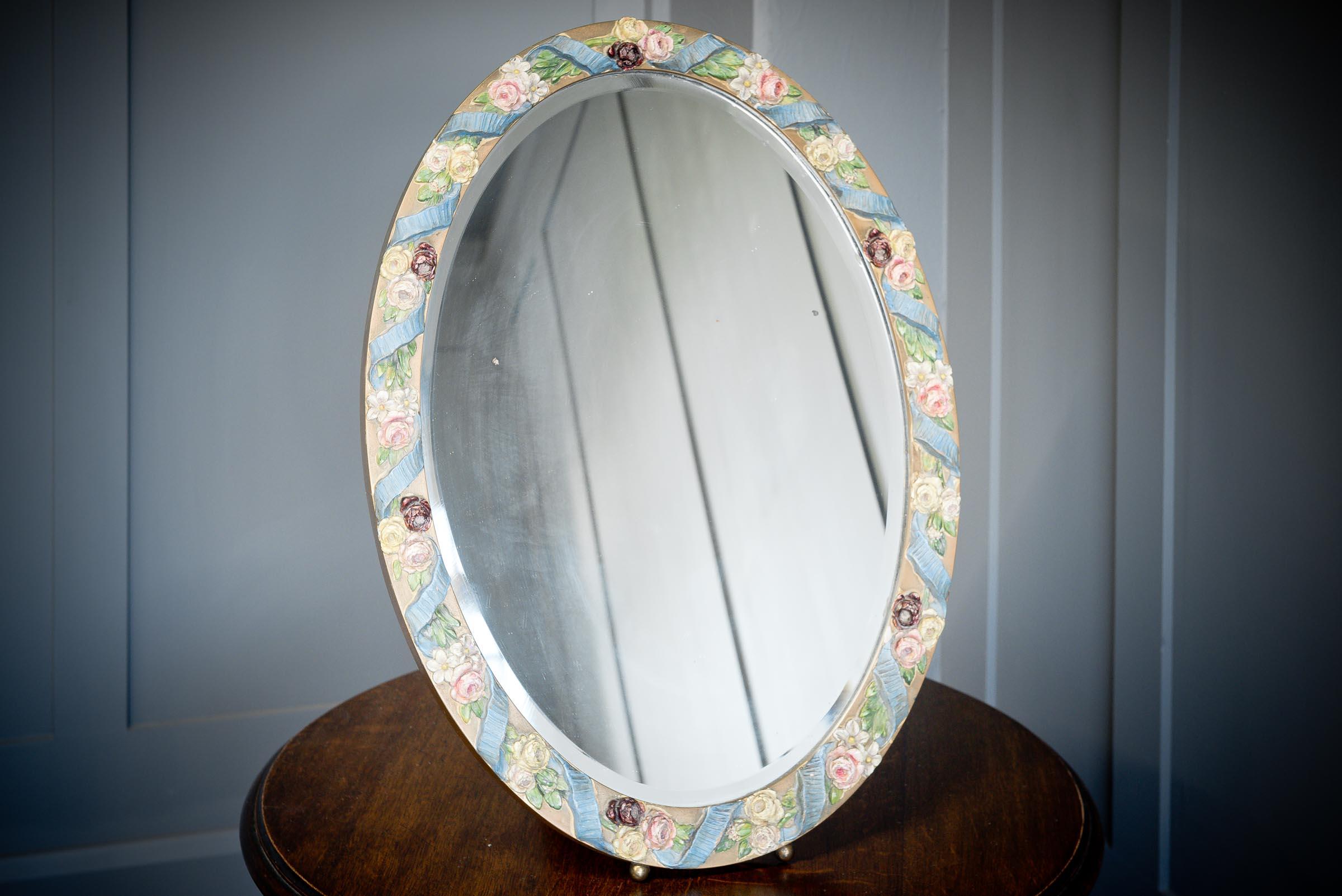 This decorative oval mirror is a typical Barbola style mirror with an intricate plaster foral frame, painted in delicate pastel colours. Popular in the 1920s, Barbola is gesso work decoration common to lots of items including fire screens, trinket