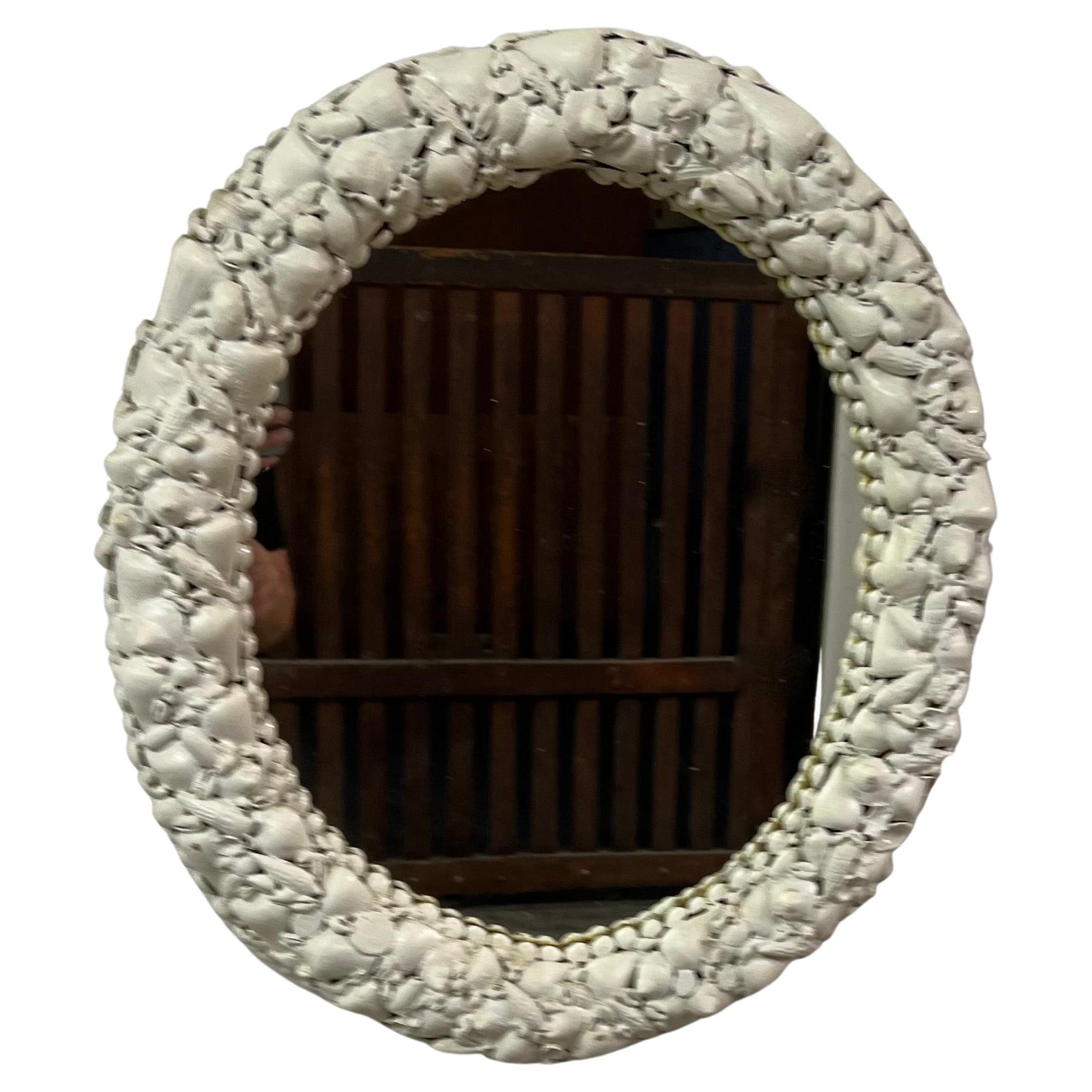 Oval wall hanging mirror with white shelf detail. This mirror is surrounded by hundreds of white shells. A wonderful addition to any room, particularly nice for seaside or beach-themed homes.