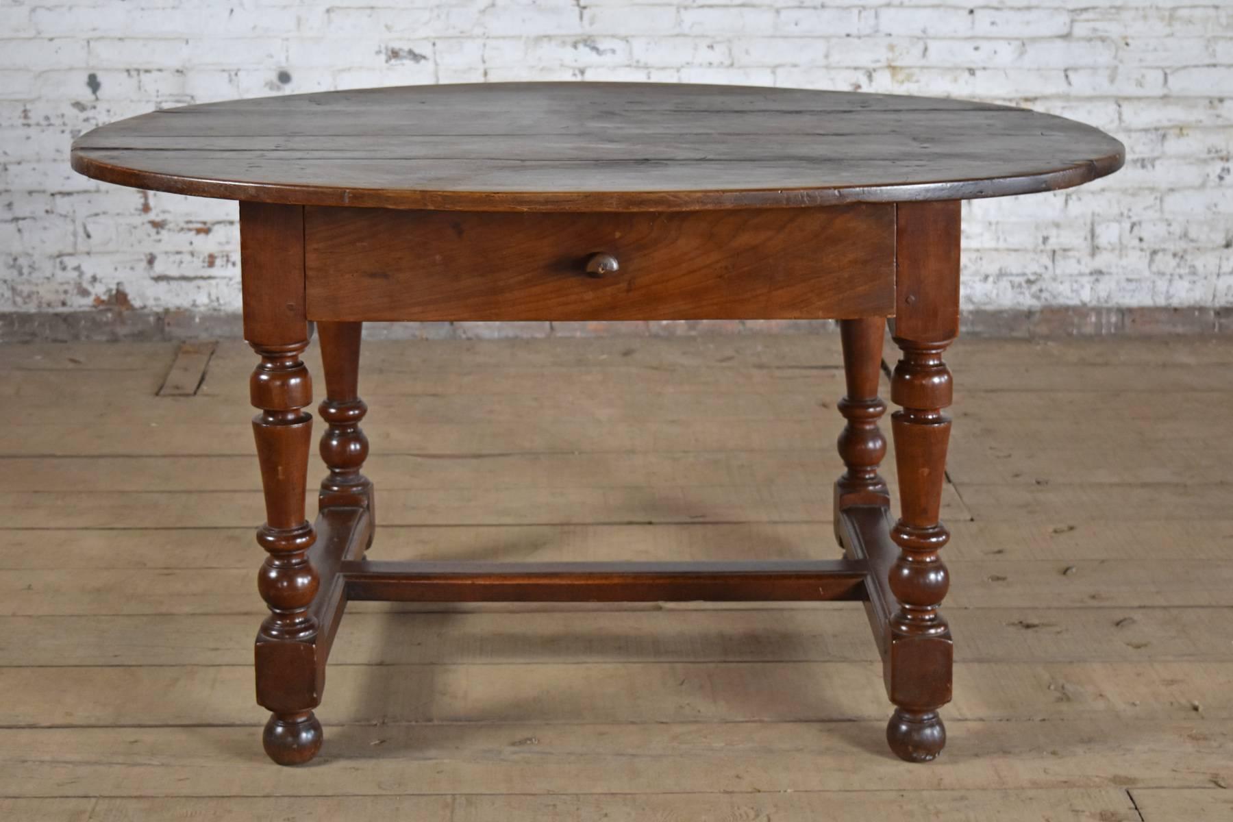 Rustic, bold, solid Walnut Table with an Oval four-board top, the frieze containing one drawer, rectangular base with four strong turned legs joined by flat H-stretcher, resting on bun feet. Deep color and rich patina. Pegged construction.
