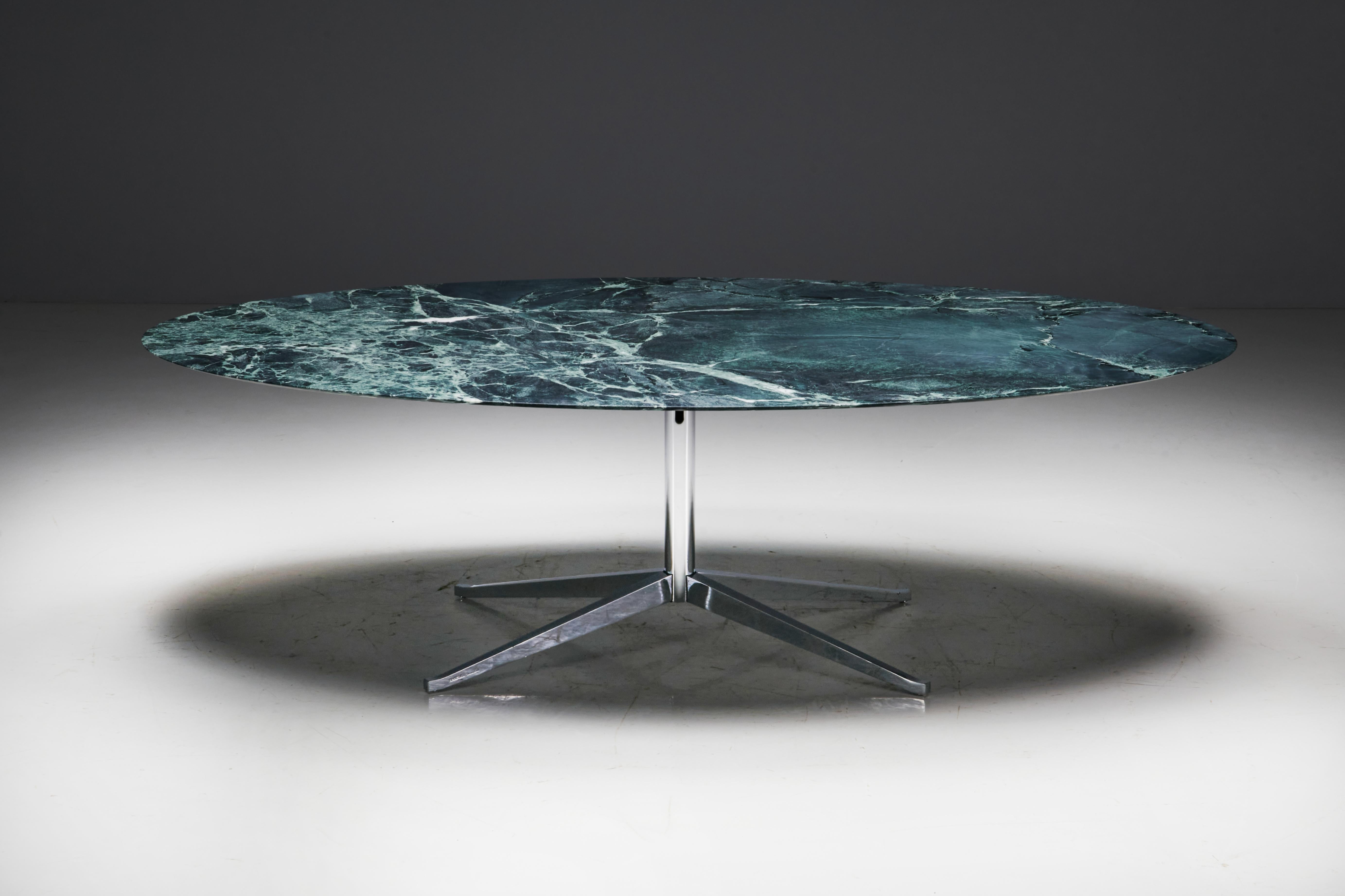 Fabriquée aux États-Unis dans les années 1960, cette table de salle à manger ovale conçue par Florence Knoll présente un design intemporel. Le plateau, sculpté dans un marbre vert massif, repose gracieusement sur une base en acier soutenue par
