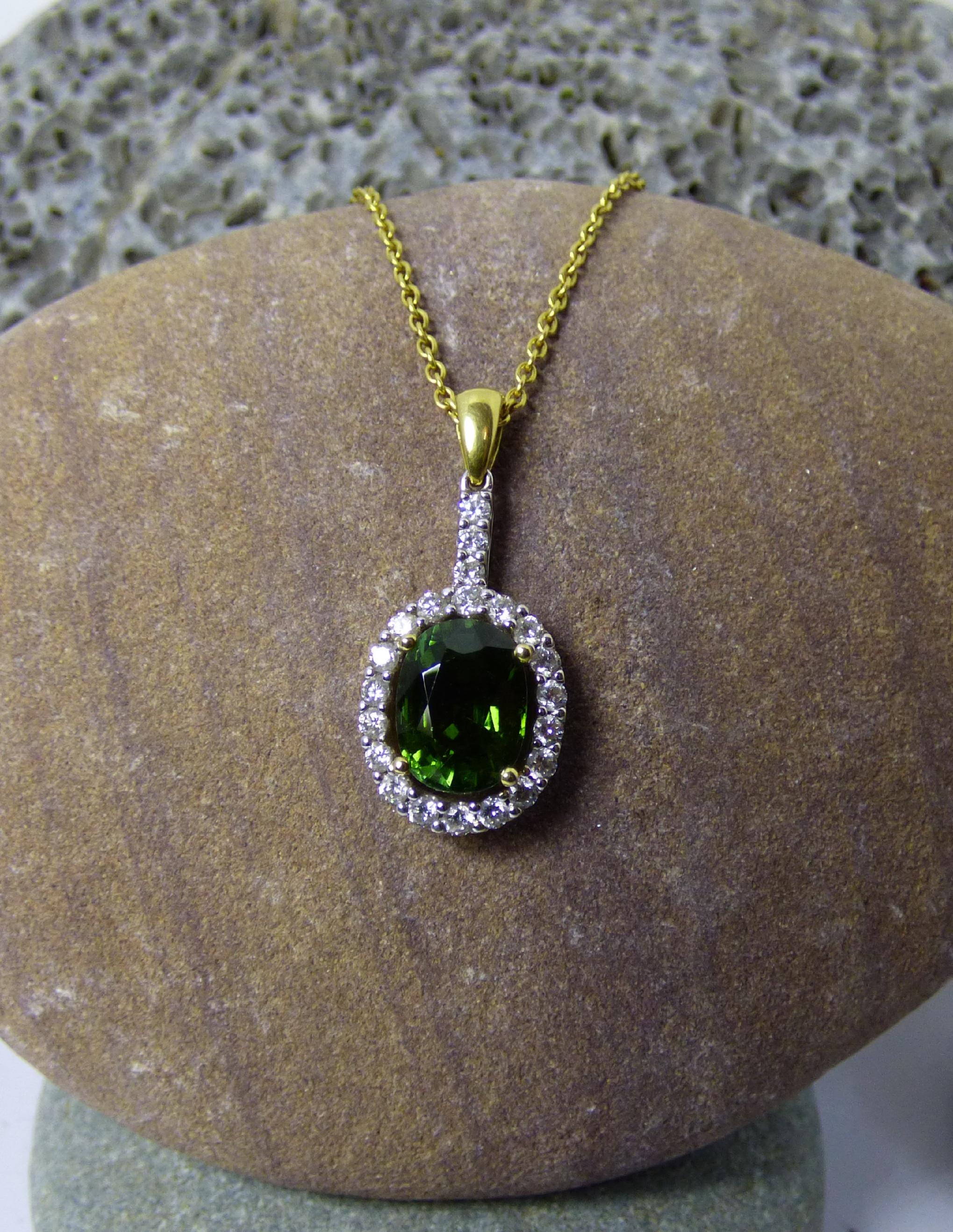 A bright and colurful green Tourmaline 12X9mm, weighing 3.94ct is surrounded by 18 Diamonds and three Diamonds up the stem. Total Diamond weight is.80ct.  The total length of the pendant is 35mm and 13mm wide.  The pendant is handmade in 18K  white