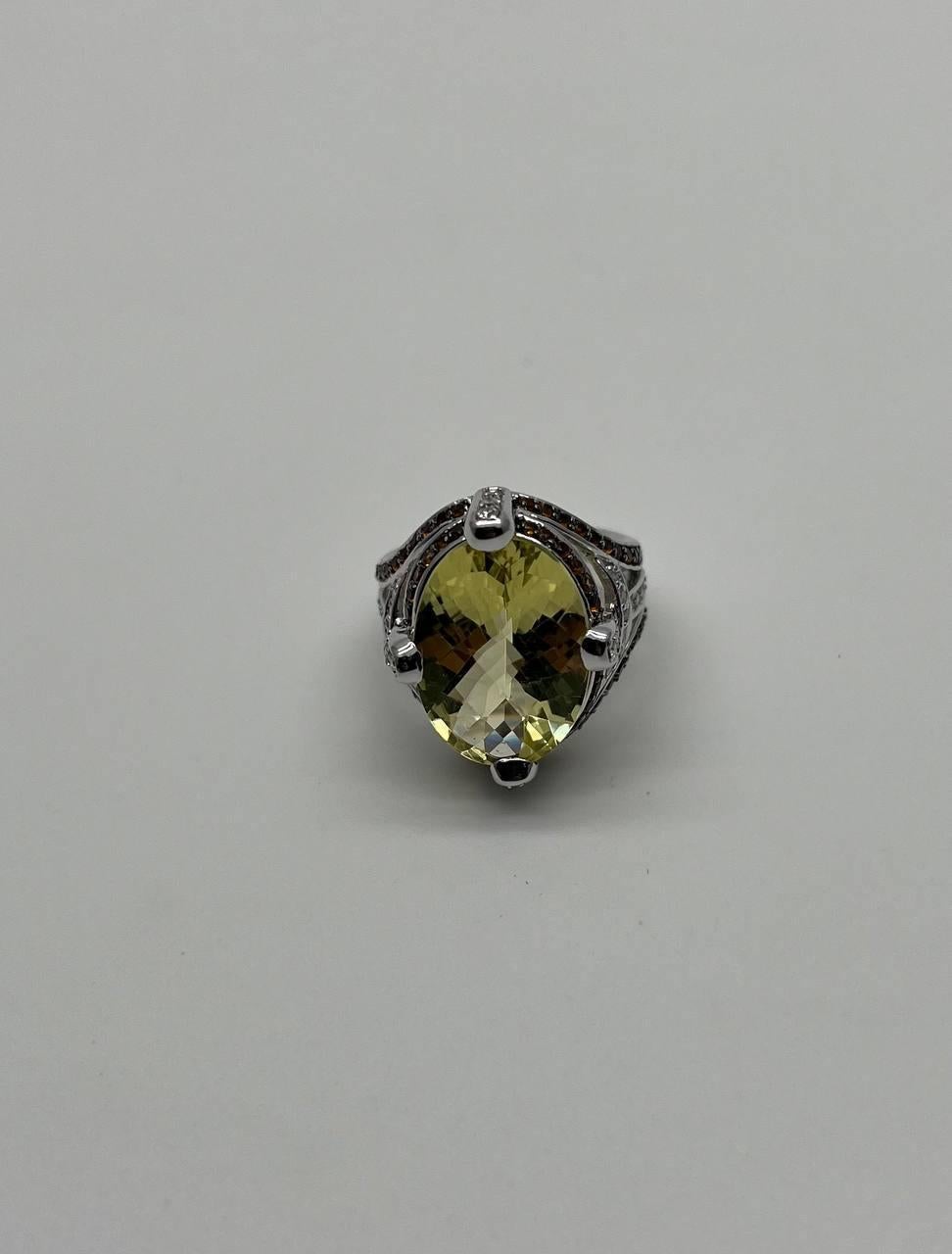 This exquisite ring features a striking oval-cut yellow Lemon Quartz set in a detailed 18K white gold band. The gemstone is secured by four prongs, enhancing its brilliance. The band is adorned with intricate detailing, adding a touch of