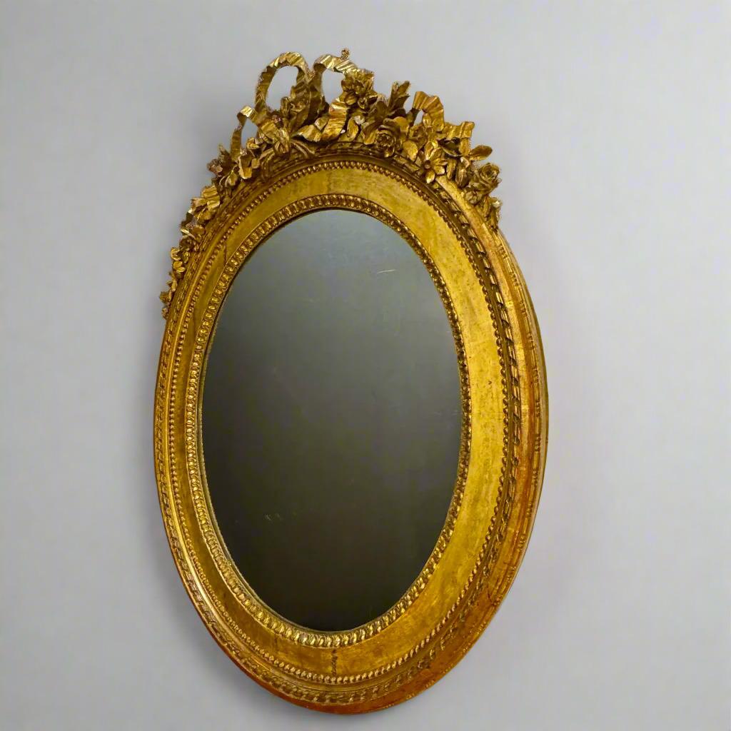 Miroir ovale en bois doré Louis XVI avec un motif de ruban (dans un nœud à trois boucles) sur le dessus et des détails floraux sculptés.