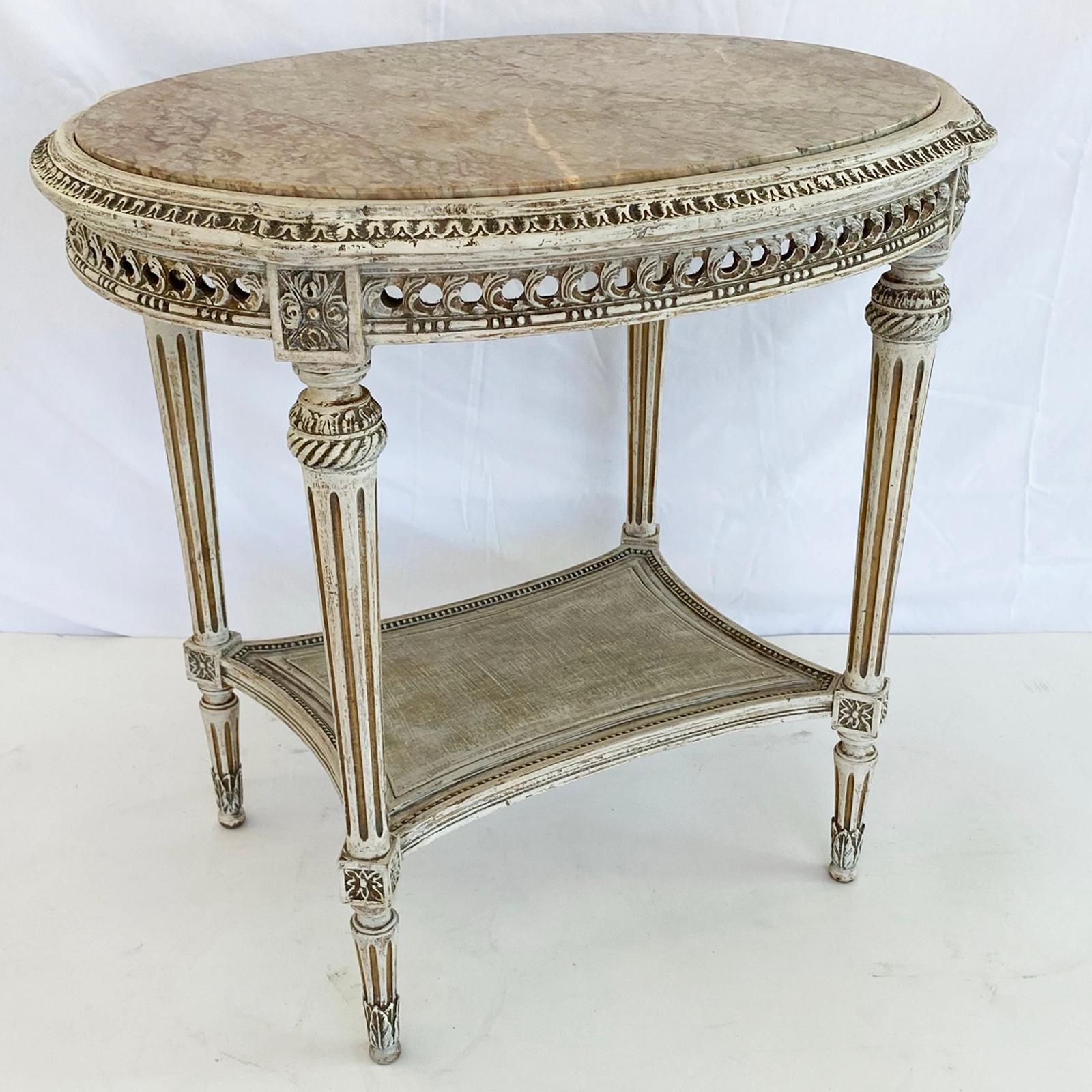 Oval occasional table, its painted finish showing natural wear, having a marble top inset on conforming table base, with gadrooned border, over pierced evolute scroll apron, raised on four, rosette-block headed, round, tapering, fluted legs, joined